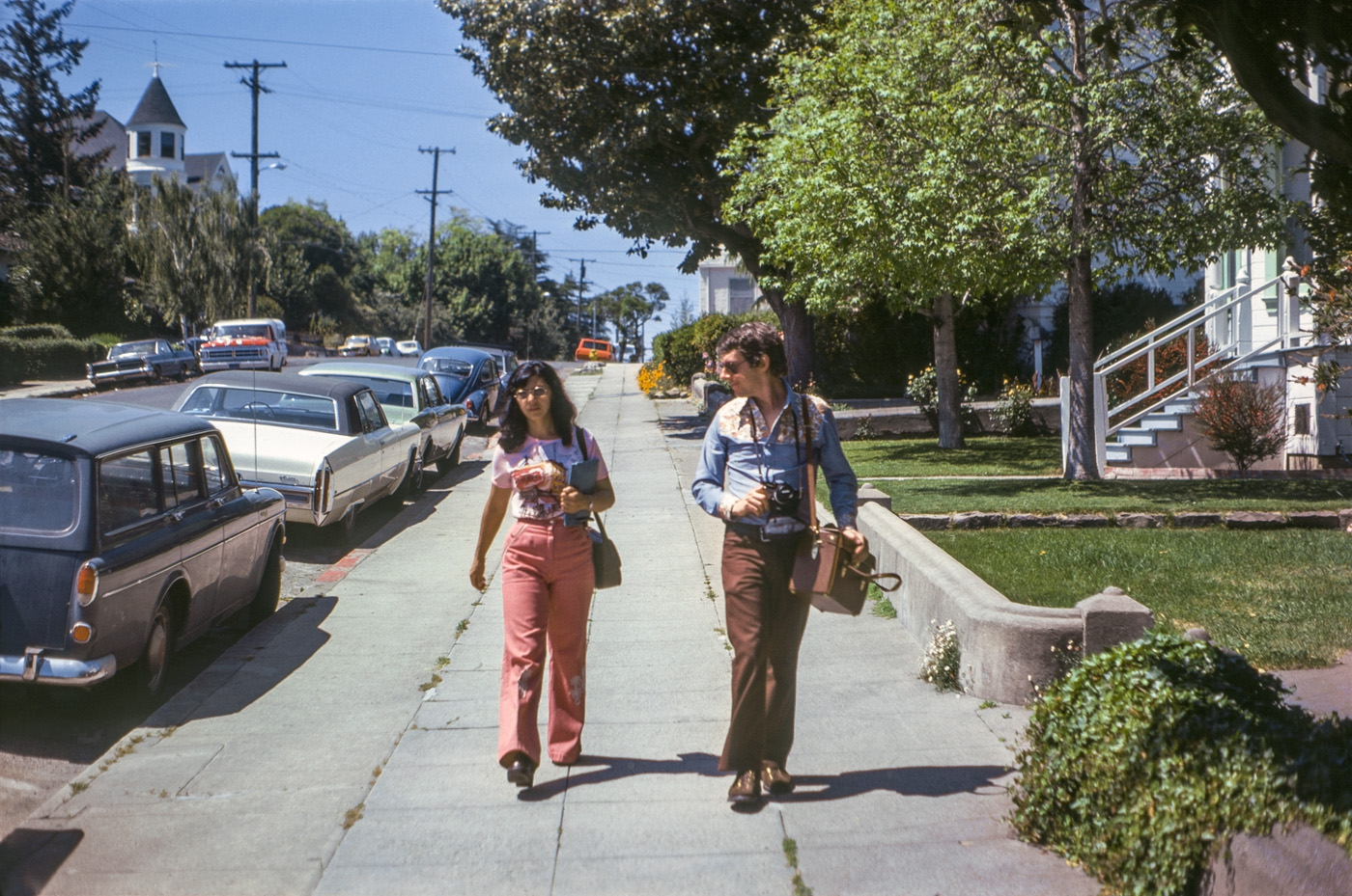August 1975. My friend snapped this Kodachrome of his wife and me strolling along the 200 block of Keller Street in Petaluma, California. I'm decked out in my 70s-style duds, including bell-bottoms, waffle stompers, whatever you call that kind of shirt, plus my Konica Autoreflex T and camera bag, she in her Petaluma tee shirt, and Keller Street in Victorians, Volkswagens, Cadillacs and Pontiacs, not to mention the ubiquitous Ford F-150 pickup. View full size.