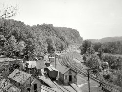 New Jersey circa 1900. "West end of tunnel, Manunka Chunk." 8x10 inch dry plate glass negative, Detroit Publishing Company. View full size.
Railway ExpressAdams Express, and probably United States Express along with five or six other freight companies, were merged by the government into the Railway Express Company. This was done on 1918 to make sure the railroads and the freight carriers would run smoothly during our participation in WWI.
Nowadays:The tracks were removed in 1942. But the tunnels are still there. Take a look:
http://www.stuofdoom.com/manunka.html
Looks like a model railroad layoutIt has a tunnel, little houses, little phone poles, lots of switches and small hills. All it needs is some small people.
Onomatopoeia"Manunka-chunk, manunka-chunk, manunka-chunk" followed by a "whoosh" of compressed air escaping as the brakes engage
Little PeopleThere IS a little person sitting on the handrail in the lower right corner.
When in ButtzvilleBrenda, it looks like you can take Route 46 there (unlabeled red road line on map). And if you waited until 1944, you could have had a great hot dog and a frosted mug of birch beer at Hot Dog Johnny's. The train may be gone, but HDJ's is still there and still one of the best hot dogs around.
http://www.hotdogjohnny.com/shop/
Just try to ignore the fact you're eating hot dogs in a town called Buttzville.
The train has left the stationThis station, built shortly after the previous one burned down, was closed in 1912 when the line was bypassed. And then the very next year it was swept away in a flood!
A short history of Manunka Chunk:
http://dlw-oldmain.tripod.com/manunka.html
Next stop ButtzvilleHow else are you going to get to Buttzville if you don't take the Manunka Chunk spur?
1942 USGS map:

No WayThere isn't a model railroader in the world who would have place a tunnel entrance that close to buildings like that! It's not realistic.
RRRRRRR!!!!!Down in the lower right you can see a flowerbed in the shape of an R. It probably spelled out D&amp;LWRR at the platform.
Bel DelThat line going down the side of the hill to the right is the PRR's Bel Del branch.
(The Gallery, DPC, Railroads)