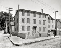 Portland, Maine, circa 1900. "Longfellow's birthplace." The home where Henry Wadsworth Longfellow was born in 1807, when Portland was part of Massachusetts. Off to the right, in front of the Block Shop: Two Shortfellows. 8x10 inch glass negative, Detroit Publishing Company. View full size.
Watch Your StepI hope there is another entrance to the place next door because that first step at the door we see is a doozy.
Blowin in the WindI like the ship weather vane.
AntennaI am not sure of its exact location but there seems to be an antenna on a roof top near the telephone pole on the right If so, what in early 1900's would it hope to receive?
[Airwaves. - Dave]
Anecdotal evidence
The house, which faced the harbor, stood on Fore Street, then a fashionable part of Portland.
In later years the house where Henry Wadsworth Longfellow was born was a tenement occupied by Irish families.
During that period, it is said a Portland schoolteacher asked her class, "Can you tell me where the poet Longfellow was born?"
A small boy answered, "Yes'm, in Patsy Connor's bedroom."
The house was torn down in 1955.
Source: Maine Memory Network
About to Fade AwayThe "Block Shop" was probably a source of rigging blocks for sailing ships, a business already in eclipse in 1900.  The ship-rigged weathervane is appropriate.  Not only did such ships require over 100 blocks to handle control lines, but to the people buying them, it mattered which way the wind was blowing.
Another neat detail in this photo is the corner piece of the sidewalk, which seems to be a single piece of stone with the storm drain carved into it rather than a poured concrete thing such as would be used today.  New England was always well endowed with stone, especially hard-to-work granite.
161 Fore StreetIf that's the correct address, then a Residence Inn sits on this spot now.  What a shame that the city didn't hold onto this piece of history.
(The Gallery, DPC)