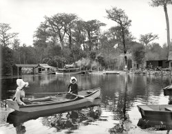 Florida circa 1902. "Silver Springs on the Oklawaha." Don't forget your flotation bonnets! Photo by William Henry Jackson, Detroit Publishing. View full size.
I&#039;m Wide AwakeAnd I agree with Slump; this picture has a curious dream-like perspective to it. It's as if the figure in the background is the actual subject of the shot and the ladies in the boat just happened to be there. He seems to be posing for the picture too as if he knew he was the focal point.
It looks like a still from a movie.If that movie was made by David Lynch.
This gives me an ideaFor a comic strip set in a funny-named swamp with animals getting into hilarious situations, topical satire, and flat bottom boats bearing different names.
Looking for the yearling...One of those ladies might be Marjorie Kinnan Rawlings, searching out her muse.
Movie?My take on it is David Wark Griffth filming Lilian Gish in her prime.
Hatted and coiffedWell, at least the hats don't look silly.  You could hide cannonballs under those things.
That guy on the roof of the boatIs looking really hard for a glimpse of wrist!
That man in the backThat character in the background sitting on the canopy (?) of that boat (??) looks like he might have jumped straight out of a Toonerville Trolley cartoon.
Flotation DevicesLooks like the lady on the left has more than just her bonnet to keep her afloat unless that's just the wind.
I&#039;m off to bedAnd this photo has the makings of a very odd nightmare.
100 Years LaterNow there's your nightmare.
Where&#039;s the sweat?Something always puzzles me about these things. Florida is so hot and humid almost year round yet in the old photos people are always dressed so hot.. I break out in a sweat just looking at this one ... did they not perspire?
[Florida was a winter resort -- not many people went in the summer. As someone who was born in Miami and grew up in Florida, I can assure you that it's not "hot and humid almost year round." - Dave]
HeadgearI love those ancestral sun bonnets that add to the peaceful look of the women in this picture. The only place we get to see one today, is occasionally, on a baby in a pram.
We have met the enemy and he flings poo. The comment by "Walt Kelly" isn't too far from the truth, with a cast of characters suitable for lampooning.   Substitute 'flat' for 'glass' bottom boat (where it was invented), consider that Tarzan made an appearance, and how the story goes that a scenic boat promoter in the 30's let monkeys loose on an island not knowing they could swim, leading to roving bands of them along the river to this day.
Boiling hotWhat always strikes me about pictures of this era is how white the whites are.  These bonnets practically glow!  Even when photographed in the woods, on a train, at the beach, etc., these ladies all looked immaculate.  Testimony (I guess) to lots of boiling water and scrubbing.  I can't make it from my house to my car in white pants without having to turn around and change. Yipes.
Fish CampThis is great! With better-maintained boat houses, a big wide dock with picnic tables and-of course-modern fashions, this could easily be any of the present-day "rustic" fish camps up and down the St. Johns River and lots of other places in Florida. All you need to fill the shot are some egrets and herons and a manatee floating by.
(The Gallery, Boats & Bridges, Florida, W.H. Jackson)