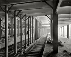 New York circa 1904. "14th Street subway station, construction." 8x10 inch dry plate glass negative, Detroit Publishing Company. View full size.
Makes you wonderHow many people were transported over these tracks since 1904. 
Side platformsPart of the 14th Street IRT station was shut down within five or six years of its 1904 opening.  It was originally built with six platforms to serve four tracks: two center island platforms to serve the express and local trains in each direction, and two side platform to serve local trains only.  The island platforms are clearly visible in this photo, and one of the side platforms can be glimpsed at far left.  In 1909 or 1910 (there's some doubt), extensions to the island platforms made the side platforms unnecessary and they were closed and walled off.  Even today, however, it's possible to see the edge of the uptown side platform when there's no 6 train in the station to block the view.
Amazingly sharp photoespecially when one considers that it is underground.
BillionsAccording to Wikipedia, the IRT East Side is a very busy line, carrying 1.3 million passengers a day on its 4 tracks. This equates to about 500 million riders a year. Assuming some ramp-up since the line opened in 1904, we can still suppose 30 to 50 billion passengers have ridden these rails. 
14th Street&#039;s Grueby Faience TilesSome of the station's custom Grueby Faience tile signage and mosaic wall decorations are just visible at the far left of the photo. Remnants of these decorations still remain on some of the much-altered platforms. A detailed construction and usage history of this station is available at http://www.columbia.edu/~brennan/abandoned/14st.html

A familiar sight, even today...I cant tell you how many times I've switched from the IRT Express from Times Square to the Local here to get down to Sheridan Square at Christopher Street in the West Village and vice versa.
The LightYou can see in this picture just how much light there was in the stations under their original design that included glass lens lighting vaults admitting natural light through the sidewalks above.  Alas, in just a few years these vaults would be replaced by ventilation grates with the light blocked by rain pans and blowers, and the only light in these urban caverns would henceforth come from electric bulbs.
Come upstairs,the weather is fine!
Captures a lot of sadness.This photo captures the essence of New York, in that all began with dust, and will end in dust.
I spent far too many days on this platform, traveling to attend a dying relative.  Very mixed memories.
Excelsior!Note the strawlike packing material in the crate. Way before they invented those damned styrofoam peanuts.
(The Gallery, DPC, NYC, Railroads)