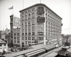 New York circa 1906. "14th Street Store." Several subplots here, involving roofs, windows and hair. Detroit Publishing glass negative. View full size.
Eye SpyI think those two lasses in the window have spotted the camera.
MonumentalLove the building with the sign on the side. It's hard to make a skinny, monumental building. It doesn't look like it's over about 30 feet wide.
Window Cleaner&#039;s ChoiceYears ago I lived on the eighth floor of a an apartment building in Manhattan that was built around the time this photo was taken.  The windows were equipped with iron rings for fastening a window washer's safety belt, similar to rig this gent is using.  When I asked why he balanced himself on the ledge of the window instead of using the safety belt he had with him, he replied that he would rather trust his sense of balance than the 90 year old rings. After a closer inspection of the rings, I had to agree with him.
Widow, er, Window WasherMan, it would kill me to have been that poor window washer.  At least he probably talked to the girls on his way up!
Human Hair Goods?Eww. No thanks.
Building maintenanceNowadays the only place you see regularly-scheduled painting of structural gingerbread is at Disneyland. Don't recall ever seeing a Human Hair Goods store on Main Street, though. An E-ticket attraction that never was. 
TodayThe "Busy Corner" building is still around today, as are some others including the very skinny one (no longer with a human hair dealer, alas). The El is long gone, however.
How marvelous!The entire building is still there, although now it is an Urban Outfitter. The 4-story building getting its gingerbread painted is also still on the street. The elevated streetcar, though, is gone, replaced by the IND, which opened the underground station at 6th Ave and 14th St in 1940.
When you look at the store selling "Human Hair Goods," just imagine it as the place where Delia sold her hair in O. Henry's "The Gift of the Magi." It was written in the same year, 1906, and just a few blocks uptown, at Pete's Tavern, at 129th E 18th St.
Great photo of one of the world's great cities, at a time when it was becoming  an indelible part of the American imagination.
The Corner todayThe West side of the facade is missing two entries (the big arches on the right of the photo), but everything else about the building looks pretty much the same.
View Larger Map
Human HairThree of my granddaughters have donated about a foot of their hair to an organization that supplies  hair to make wigs for child cancer victims. I guess O. Henry's Delia has nothing on them.
Sharp ShotFull of interesting detail as it is, this photo is also noteworthy, to me at least, because of how beautifully sharp it is in a technical sense. You can look at almost any part of it and see amazing details.
Some window washers still use that rigI worked at a place two years ago that had those hookups outside each window, and sure enough a fellow came by once a year to climb out and use them. He smelled of alcohol, and I hardly blame him!
Macy&#039;s was thereThe skinny building was also once Macy's, though I don't know if it was before or after this photo. The tracery of the Macy's name can still be seen under the paint over the front door. The building is now owned by the New School University. 
The large building on the corner is a high-end condo building now.
Henry Siegel&#039;s FateI believe the structure in the foreground with its gingerbread being painted is actually the elevated station. The station building on the other side of the tracks matches it.  
All of the Henry Siegel's  14th St. Store buildings are still there, although the shorter middle building has had an apartment structure built on top of it. The corner building is now filled with (what else?) luxury condos.
Alas, the story of the 14th St. store itself did not end well for Henry Siegel. It lasted only a decade, and ended with Siegel going to jail. He would end up living in a boarding house in Hackensack.
More of the story can be found in this 1999 NY Times article.
The sliver buildingat 56 west 14th street was vacated by Macy's when they moved uptown to 34th street in 1902.  With a good eye one can see the Macy's star logo on the facade still today.
http://www.nytimes.com/2004/05/30/realestate/streetscapes-readers-questi...
Wigs, glorious wigs...From the Brooklyn Daily Eagle, September 22, 1875
Wowsa!!So much to look at.  What a great picture - this is one I could keep coming back to and still see something new.  Thanks, Shorpy.
Human hair?  Good store!The human hair store doesn't bother me a bit.  Hair was commonly used in beautifully woven and braided jewelry in the 19th century.  (I've tried to copy the technique with my own hair - it's difficult!)  Women also bought human hairpieces and extensions, much as they do today.
I'm adding this photo to my Shorpy all-time favorites.  So much to see!
Can&#039;t decideWhat intrigues me more.  Is it the skinny building with all the ornate work, or the sign "Dry and Fancy Goods"?
Piggy Bank from the 14th Street StoreI am soooo enjoy this site.  Back in the 1970s as a teenager, I inherited a small "piggy bank" with a serial number, 55738, on it.  It is a heavy metal woodgrain lockbox four inches wide with a carry handle on it. No key. Printed with copper-like inlay: "The 14th Street Store 6th Ave's Busy Corner, New York, Henry Siegel, Pres." I would love to know who used it, what they were saving money for, and the value of the box today.  I am now in my fifties and still proudly display my antique box.
[This would have been used in the store by cashiers or clerks. - Dave]
The Bank BoxSo I just wanted to comment on the little bank picture that was posted. The box was a giveaway that the store had. Bank in those days a lot of department stores also contained banks. That box was a giveaway for children when their parents would open accounts. 
I did a bunch of research on the one I have just like it!
[The box below is not a "giveaway." - Dave]
We have a 14th Corner Store Bank Box too! My husband was given one of these bank boxes to him by his Grandmother and now the bank is being passed down to our 10 yr old son. I would love to pass on the history of this box to him as well. What an interesting box. The box displays serial number 92743, and looks a little different than the one pictured below. It does not have any engraving on the top other than that of the serial number. Looks like the one below has some words engraved on the top where my serial number is located. 
Does anyone know anything more about these boxes? 
Macy&#039;s Sign When I walked by 59 West 14th on Wednesday scaffolding was up.  Looking at the building yesterday the tracery of "Macy's" has been painted over.
Macy&#039;s mysteryBut what in the world is this guy up to?  Tying his shoe?  Scraping something off his shoe?  Taking a shortcut off the El platform?
(Thanks to Cosmopolite for bringing this brilliant, busy photo back to our attention.)
(The Gallery, DPC, NYC, Stores & Markets)