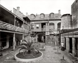 New Orleans, Louisiana, circa 1906. "Old French courtyard on Royal Street." 8x10 inch dry plate glass negative, Detroit Publishing Company. View full size.
It&#039;s still there.Courtesy of Bing's Bird's Eye View and Google Streetview:  this is 729, 731 and 733 Royal Street, New Orleans.
The cistern is gone, the awful enclosed porch over the tunnel has been removed and the neighborhood seems to have gone more upscale since 1906 but the building survives in fine shape.
Potato patioToo poor to paint, too proud to whitewash?
AccretionReminds me a little of how corals build a reef.
Sisters a-courtingThere's a popular restaurant in New Orleans by the name of the Court of Two Sisters. This isn't it. 
Thinking of that name compels me to name this photo the Court of Five Sisters. There's four women to be seen and that water tank is a ... cistern.
You can tell it&#039;s Frenchby the plumbing.
Porch railingOn the upper left. It took me a long time in looking at it to realize why it looked like it was leaning outwards instead of straight up and down. It's the stays, not sure if that's what they're called, that are placed at an angle instead of up and down. 
Creole TownhouseThe planking on the facade is a late extension.  Are those stables on the right?
Stella!Sorry, couldn't resist.
(The Gallery, DPC, New Orleans)