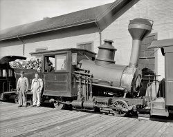 Circa 1906. "Engine, Mount Washington Railway, White Mountains, New Hampshire." The little engine that could also serve as a portable pizza oven. 8x10 inch dry plate glass negative, Detroit Publishing Company. View full size.
New Hampshire&#039;s Cog Railway"The Cog" as it's known has been (during the summer) delivering passengers (mostly tourists) to the summit of Mount Washington since July 3rd 1869.  Soot spewing coal fired boilers have been largely replaced with cleaner diesel units, although coal is still used on  some early morning ascents.  The boilers are canted as in this photo so that they'll be level during the steep ascent and descent.
[You'll note that this engine is not coal-fired. - Dave]
[I did notice that Dave.  However, coal has been the railroad's solid fuel choice for a number of decades. - Mal]
The weather on top of the summit can be among the most severe in the country and is where the world's record wind speed of 231 MPH was recorded.   Hence the mountain's timberline is at only 4,000 feet.
Train quesitonProving I know very little about trains. Is it supposed to be stuck up in the air that way?
Railway to the MoonThis engine served on the cog railway that still ascends to the 6,288 ft summit of Mt. Washington. It is the oldest rack-and-pinion rail system in the world (1869). Before construction, the project was derided as a pie-in-the-sky "Railway to the Moon." So it truly was the little engine that could!
The numeral 1 on the engine identifies it as the rebuilt "Mt. Washington," originally named "Falcon." Incredibly, it's still sitting in storage in the shops at the rail yard at the foot of the mountain.
KilroyThat's probably his first appearance, behind the tender.
That bend?T'was like that when we took it out dis mornin'.  Honest.
Not On the Level!The reason the locomotive boiler is on a 'slant' in regards to the frame and cylinders is that when the locomotive is working and climbing on the way to the summit, the water and firebox within will be more or less horizontal on the grade.
The large dome accumulated steam well above the level of the water.
As wood was the fuel, a long smokestack with a large opening at the top which is covered with a screen was applied to catch sparks and help prevent fires along the right of way.
The screen has a latch so it could be opened.
Wood is easy to fire, burns clean, and leaves little ash.
Coal has more heat value by weight, and was used in later years.
Unlike most of the other locomotives featured on Shorpy, this one does not need sand for traction nor has piping or a sand dome for sand application.
The spoked locomotive wheels riding on the rails are not powered, the movement supplied by large pinion gears driven by the four external steam engines, the gears' teeth mesh with the teeth on the horizontal rack between the running rails.
The teeth of one of the 'cogs' or pinion gears can be seen above the front spoked wheel and frame.
There appears to be a band-type friction brake below the front coupler operated from the cab by the long reach rod and lever.
The operating handle for an injector to put water into the boiler can be seen inside the cab side window.
Thank You.
Leaning Into the WindThese cog railway locos have slanted boilers because when they are climbing the hill, they want to boiler level to prevent "priming", that is, water getting into the steam pipes (very bad). The Pikes Peak locomotives were similarly slanted.
[In other words, the boiler is level when the engine is ascending or descending the grade. Note that the passenger car stays on the uphill side and that the loco always faces "up," with descents made in reverse. - Dave]
Kilroy was here?I wanted to see Kilroy so bad that I ran my computer up to 400+ on the zoom and still couldn't find him. Oh well, I love this cog railroad and it is definitely bucket list worthy.
Dave, thanks for the location pic and I don't know how I missed this guy.
One of the neatest trips in North AmericaI am lucky to have been able to take this trip three times. All with steam power. One one trip; we hiked to the Lake of the Clouds Hut, and back. Awesome views. My last trip, we saw snow at the summit in late July.  The TV station was still broadcasting when I was there. The weather guys up there were fascinating. Everybody should do this once if you can.
ThanksThanks to everyone for your input. This is why I consider Shorpy such an education in so many areas.
Fond memories of a trip up Mt. WashingtonThe summer I was 13 I rode the cog railway up Mt. Washington with my parents and brother. On the way up my brother &amp; I stood in the aisle of the car and found ourselves leaning forward at such a steep angle I thought I'd pitch forward on my face. We also visited the famous flume. What great fun! I loved New Hampshire.
Thanks for the memories, Dave.
(The Gallery, DPC, Railroads)