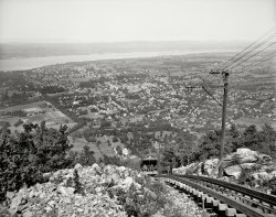 Dutchess County, New York, circa 1905. "Mount Beacon Incline Railway, looking down, Fishkill-on-the-Hudson." 8x10 inch glass negative. View full size.
Max Elev.Immediately brought to mind "High Tor" by Maxwell Anderson.  
Signal wiresI noted the left pair of wires suspended under the brackets on the poles. I worked in a coal mine for a while in Colorado, which was on a steep slope and had a similar inclined track, but underground. The "conductor," if you will, had a long wooden stick with a metal bar mounted across one end. He could signal the hoist operator on the surface from any point in the incline by basically shorting out the two wires above us, which rang a large gong signal in the hoistman's cab. Basic signals were one bell to stop, two to go up, three bells to go down.
[Or would he be closing the circuit rather than shorting it. - Dave]
Dave:  You are correct ......
Get your lean on!Look how far forward that fellow in the front is leaning. Really puts the grade of incline in perspective.
The OtisThe two towns below were Matteawn and Fishkill Landing, incorporated into the city of Beacon in 1913. This was one of two great "Otis Inclines" built in the Hudson Valley by the elevator maker. The other served the Catskill Mountain House from the Palenville rail connection to the steamboat  landing at Catskill.
Great place to hikeThe incline railroad was active from 1902 to 1978. The land is now preserved as Mount Beacon Park. Hikers up for a strenuous workout can climb a staircase and then huff and puff up an eroded woods road to the top.
There is talk about rebuilding the railroad. For now, only the shell of the powerhouse remains. Great views are still available from the top:

Acrophobics AnonymousAnyone have their number?
Gone but not forgotten.Seems to have been completely destroyed by a fire in 1983 but there is interest in it still.
http://www.inclinerailway.org/index.html
The Secret Of Its SuccessThis railroad was a hit with its passengers because they were so inclined.
Take a ride down Memory LaneIn this video clip.
Name ChangeThe former Fishkill-on-the-Hudson is Now Beacon. There is still a Fishkill, but it's a mile or so to the east.
PriviesLove the outhouses!
I think I&#039;m spotting a trendI'm amazed at the popularity of incline railways at the turn of the 20th Century. Growing up in Southern California, we always heard about the long-dismantled Angel's Flight, and I just assumed it was unique. Certainly there, or in Cincinnati, it served a practical need, but I find it striking the number that were constructed for pleasure purposes, as this one clearly was. Hard to imagine such a capital investment today.
From across the riverI was born and raised in Newburgh, just across the river from Beacon, and recall as a kid, hiking up Mount Beacon at least twice. Those excursions involved a bus ride from my house down to the ferry terminal, the ferry ride over to Beacon, and a long walk up through Beacon to the cog railway terminus at the foot of the hill, and then trudging up the mountain to the top. A long journey, but well worth every step!
I am illuminatedDon't miss rjc's video clip below. That answered some questions for me. I was looking for the second track and had forgotten how that could work with a counterbalance car. Also, check out the guy following the car down the mountain. It looks like he is riding a device that lets him coast down the hill on either one rail or the outside wooden one. I can't tell which one he is on.
(The Gallery, DPC, Railroads)
