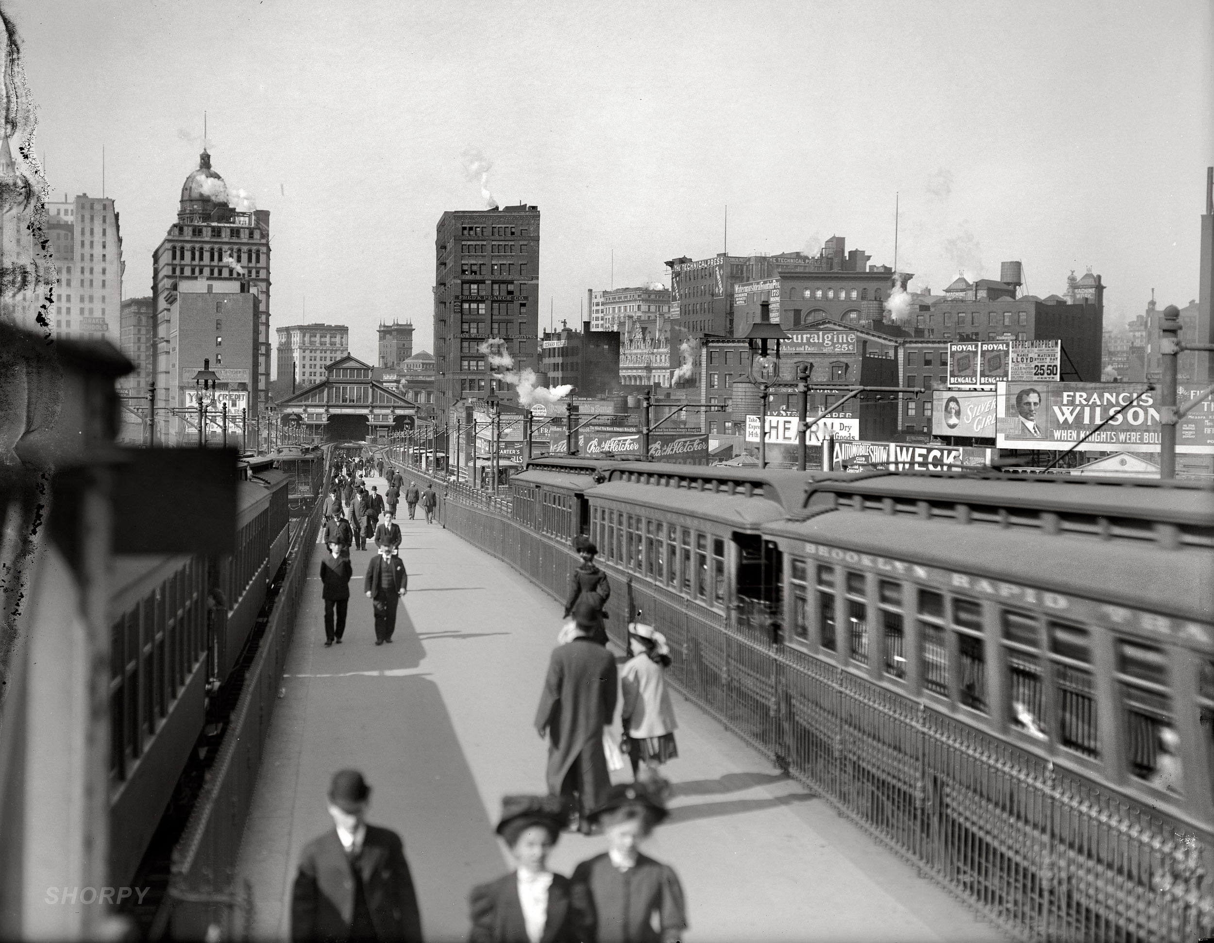 The Brooklyn Bridge Promenade and Manhattan Terminal in 1907 amid a forest of billboards facing the trains. The domed structure is the New York World building. Detroit Publishing Company glass negative. View full size.