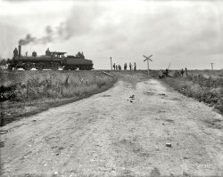 Joliet, Illinois, circa 1901. "Chicago &amp; Alton Railroad. Track elevating at grade crossing." 8x10 inch glass negative, Detroit Publishing Co. View full size.
At-grade crossingNice of the railroad to be so considerate of those traveling down that road!
Working on the railroadWhatever these guys are doing here, it looks like hard work. 
Rough crossingFrom the partly buried fence posts next to the right-of-way and the naked dirt of the visible rail bed it looks like the railroad has raised their grade around three feet or so, whoever was maintaining that road had some shovel-work ahead of them.
LocomotiveSeems like the 0-6-0 layout wasn't common in US locomotives at any time.  Could this be a specialized switch engine or something?
The Locomotive2-6-0 Prairie type.
Second OpinionA Prairie would be a 2-6-2, but in any case I don't see either a leading or trailing truck. It looks to me like an older (1870s-'80s) Mogul converted to a switcher by removing the leading truck; B&amp;O did that to one of theirs about this time. It could even have been an older American with an extra driver added.
Opinion 1.1Oops, I was wrong. I would have sworn I saw a pony truck but I would still be wrong. There does seem to be a lot of empty space in front and I'm betting you are correct that it was a conversion. this was in the days when railroads built and maintained things to last forever. It very well could be a American conversion.
(The Gallery, DPC, Railroads)