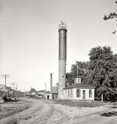 Circa 1900. "Water tower in Dwight, Illinois." Unusual columnar design with a brick base, topped off by a weather vane and lights -- a sort of smokestack-lighthouse-watertower hybrid. Detroit Publishing glass negative. View full size.
Pressure would be higherIt would be higher pressure because the pressure depends upon the weight of all the water above the output area. Although the volume of water could be the same as a short fat tank, the depth would be less in a short fat tank, hence a smaller amount of water above the output. 
A tale of two cylindersI am no expert on water-pressure physics, but it seems like a "tall" column-style tank like this would give more water pressure than a shorter, fatter cylinder of the same volume. Or is that just misleading intuitive thinking? The weight of the water would be the same, after all.
[I think your hunch is correct. The weight of the water over the drain (or water pressure, expressed as weight divided by area, for example pounds per square inch) would be greater in a tall, relatively thin (columnar) cylinder. - Dave]
Tower for SaleThere's a similar brick water tower (minus the tank) for sale in Raleigh, NC. Built in 1887, it's on the National Register. Yours for a cool $685,000.
What is that upside down funnel thingLooks to be hanging from the wires.
[It's a carbon-arc lamp. - Dave]
Also for those not used to such things, that farm implement at the base of the water tower is a mower.  Could be used for hay, or wheat or just grass.  Used my grandpa's many a time back in the '60s.
Big towerThe Fostoria, Ohio, water plant still has a base, made of stone, but the upper part is gone. It too was similar, but the water was not potable, rather only for fire suppression. Old photos show the tower was taller than the base.
StandpipeThis is called a standpipe. It is basically a large pipe stood on its end. It provides some water storage volume but is mainly used to increase the pressure in the water system without having to constantly run a pump.
(The Gallery, DPC)