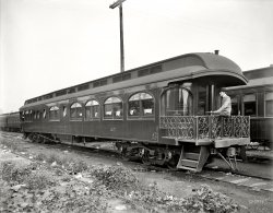 Circa 1905. "Pere Marquette Railroad parlor car No. 25, exterior." 8x10 inch dry plate glass negative, Detroit Publishing Company. View full size.
Details of CarThe following details come from the book, Mr. Pullman's Elegant Palace Car by Lucius Beebe, 1961:
Superb examples of American Car &amp; Foundry craftsmanship are these two palace cars frin the collection of Arthur D. Durbin [pictures differ from what Shorpy shows]. The Pere Marquette's parlor-cafe No. 25 was in built at A.C.F.'s Jeffersonville shops in 1903 and assigned to the Northern Michigan vacation service on trains No. 1 and 5, and Nos. 9 and 10, the Resort Special. Of this train the public timetable for 1905 of the Great Central route of which the Pere Marquette was a component, says, 'Trains No. 1 and 5 will stop at Little Manistee River (Fishing Camp) on signal,' an index of casual operation in good old summer days. The car was characterized by a curved rear bulkhead with plate-glass windows to match, giving onto an observation platform of uncommon depth.
The Little Manistee River is on the western shores of the lower peninsula of Michigan between Ludington and Frankfort.
GarbageWhat is a bit surprising to me is the amount of litter all over the ground. I'd think a railroad wanting to show off its equipment would want the best representation possible. Or maybe somebody just took a snapshot of a lone car on a siding.
[8x10 glass negatives aren't what most people would consider casual photography. Made with big heavy view cameras on tripods. - Dave]
CheersIs someone proposing a toast from yon window?
GR&amp;ILook like Grand Rapids &amp; Indiana cars in the background. Another railroad providing service to Michigan's "Sportsman's Paradise." Could be at Muskegon or Grand Rapids. I think the GR&amp;I and PM crossed paths at these cities, maybe others.
It&#039;s all in the detailSo nice to see the livery and striping details on these Cars. The flourished ends are a nice touch, tradesman at work. In our modern age it is really a treat to see great resource for signpainting restored cars such as these.
HandshakesI can't remember ever seeing a three line air system on any rail cars I am familiar with. Nowadays only one is used.
I have no doubt someone will come along shortly with a perfectly reasonable and technical explanation for us all.  
The HosesThe three hoses you see are, from smallest to biggest, the train signal line, the air brake trainline and the steam heat line. The air line for the signal connected to a whistle in the locomotive cab so that the conductor could, through a series of long or short tugs on the valve, signal to stop at the next station, supply more steam for heat, etc.
The air brake line carried 90 to 110 psi compressed air and by reducing the pressure in this line would apply the brakes throughout the entire train.
The third and largest hose supplied steam used for heating the cars, a big improvement over the coal stoves used previously which tended to ignite these varnished wooden cars rather quickly in a wreck!
Multiple HosesOne hose was the air brakes. A second was steam heat. The third may have either been for steam (connections look similar) or for drinking water.  Only the air brakes would have been needed on a freight car.
Air Signal lineOne of those extra air hoses on the end of the car is probably for the train air signal line.  The other line I am not sure about without looking at some old books I have.  The cars probably had stoves for heat and it's not the right size or type of connection for steam heat.  It seems like I should know, but I just cannot recall what the third line would be for.
Three LinesThe three lines most likely are: air brakes, steam heat and train signal line.  The signal line permitted the conductor (by a small valve located on the bulkhead) to give whistle signals to the locomotive crew.  
Re: HandshakesThanks to all who jumped right in with explanations for my previous comment. Shorpy readers are the best! No question remains unresolved very long here. I learn something new every day.
Thanks Dave, for this entertaining and educational site.
(The Gallery, DPC, Railroads)