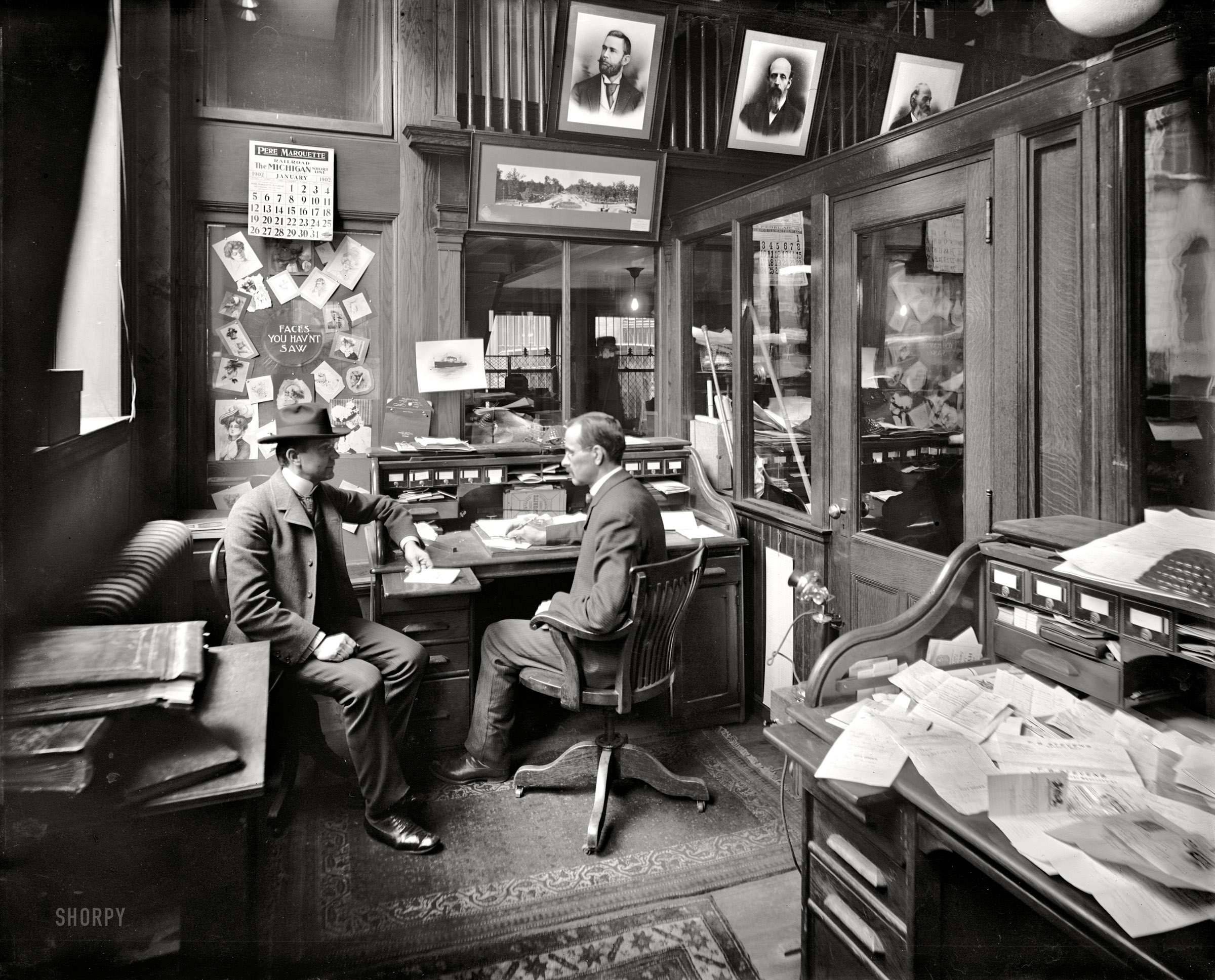 Detroit, Michigan. January 1902. "Richmond & Backus Co. office." Our third peek behind the scenes at R&B -- printers, binders and "office outfitters" -- reveals a cozily cluttered workspace enlivened by a display of "faces you have'nt saw." 8x10 inch dry plate glass negative, Detroit Publishing Company. View full size.