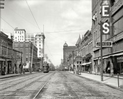 Little Rock, Arkansas, circa 1910. "Main Street north from Sixth." A zoomed-in version of this view. Note the Free Bridge in the distance. View full size.
Okay, but *why* 8:20?Does the use of the time 8:20 have any special meaning? Or is it for purely decorative purposes, like clocks for sale in shops that have their hands set to 10:10?
[At 8:20, the hands leave plenty of blank space for text. - Dave]
Ahh, city life! From the Newsie and the fellow in some sort of Uniform on the left, to the man in the window of "Jones House Furnishings," this is a wonderful image of life in 1910. 
The big clock there on the corner, in front of McKinley's Jewelery store tells the time of day (8:18 AM)( This must have been the morning rush hour.) So many of these clocks are either gone or no longer work at all.
[Shorpy veterans will recognize the clock-face jewelers sign as a familiar fixture on early 20th-century streets. They're not real clocks, and all show 8:17.  - Dave]
The East 14th St. streetcar is rolling along. (Please pay conductor upon entering car - I wonder what the fare was back then. a nickel? a dime?) 
I also see a little business competition in the Stein and Kress 5 and 10 cent stores.
The descent from the Free Bridge looks a bit steep but that could be the camera itself doing that. 
I wonder what the "LIGHT" sign above the street means...
Further to the right, in front of the E.D. Bracy Hardware store, There is a nattily dressed gent walking along. We also see some large wheeled bins marked 5 cents. I would like to see what is in those. To either side of  Bracy's hardware are a Sporting Goods Store and J.H.Martin's Arms Store.
Then comes the 'Jones House Furnishings Store' with its list of wares that you can purchase within. 
Imagine having a time machine so that you could go back and fill your home with furnishings from 100 years ago! Ready made antiques! 
A little help, pleaseI'll supply the truck if someone else will let me use their time machine. Then we can go back and get the spiked ball on top of the Stein Co. 5&amp;10 at left. It's gonna look great on my garage!
Keen KutterE.D. Bracy Hardware Co. Your Keen Kutter dealer.  This boat named for the knife, still plies the waters of Lake Winnipesaukee New Hampshire.

Remembering streetcars and trolley busesConductors on streetcars was a job destined to become obsolete as eventually the driver had to handle all the chores.
I remember one corner in Cicinnati where it was rare for a streetcar or trolley bus to make the turn without the the trolleys coming off the wires.  The driver would rush off, line them up, and we would be on our way again.
Keen Kutter IIAlive and well and highly collectible I might add.
Public Time  These jewelers clocks were very real.  During this period of time railroad, street car employees and the better off had personal time pieces and the rest had municipal, jeweler and other clocks for when they were away from home.
  These particular clocks had a pendulum that was short enough to fit in the diameter of the face ...
[The hands on this clock (below) are painted on -- it's right twice a day. Same for the other 8:17 jewelers' clocks seen here. - Dave]
  Thanks for the enlargements and setting me straight Dave.  It really shows up in the symmetry issues of the flourishes at the end of the hands.
8:18 still common at fine jewelersWhile no longer universal, that time is still the most common time watches are set to at fine jewelers, because it doesn't obscure the maker and model information.  The to couple of pictures site what I mean.  Go to any specialty watch or fine jewelers, and chances are that's the time on the face, if its not actively running.
8:20 or 1:50Those of us who remember the old Timex watch commercials where they'd torture test a watch by tying it to the blade of an outboard motor or attached it to a jackhammer or some similar method to show that the watch could "take a licking and keep on ticking," will remember that the watch usually read 1:50 - 10 to 2 - and it read that way for a reason. Like 8:20, 1:50 didn't obscure the maker's name or the model type. 9:15 or 3:45 (or worse, 9:45 or 3:15) wouldn't work because there would always be those who would claim that the watch only had one hand! As for why Timex chose 1:50, well their name was at the top (under the 12) of the watch and placing the hands at 1:50 framed the name nicely.
+105Below is the same view from July of 2015.
(The Gallery, Boats & Bridges, DPC, Little Rock, Streetcars)