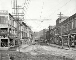 August 1910. "Main Street, Gloucester, Massachusetts." The sidewalks and signage of a century ago. Detroit Publishing Company. View full size.
It Takes a ManThe following is one of about a dozen letters in a section entitled "Women Clerks." While the men admit that women "add tone" to a hardware store and may be good at selling Kitchen Furnishings, women were deemed poorly equipped to properly clerk a hardware store in small-town 1910 America.



Hardware Dealers' Magazine, Vol 33, 1910 


Takes a Man to Sell High Priced Cutlery

We have had considerable experience with women clerks and it is our opinion that while a lady clerk is all right for passing out goods that are called for, it takes a man to sell high priced cutlery. We employ three sales ladies in the summer season, but if the business would stand it would replace them with men.  Lady clerks, however, are very useful about the store in keeping showcases and shelves in shape and keeping the store neat.
Charles J. Gray.
Gloucester, Mass.
Reminds me of a town where I lived.Turn around and you'll bump into a dentist. 
Seek, and ye shall ...It reminds me of a page from Highlights Magazine.  Find the sailboat.  Find the shoe.  Find the giant shotgun.
Tailor madeStrangely the tailor's shop is on the right side of the street and the sewing machine is above the hardware on the left. 
Singer in the windowCheck the open sewing machine in the upper left hand corner--probably a Singer.  It's more than likely been moved by now.
Two hardware stores steps from each other. Charles J. Gray and L.E. Andrews &amp; Co. still manage to differentiate themselves, though. Gray looks to have a broader selection, but I believe I'd look for the construction materials, etc. at Andrews. But this was back when American still made and sold things. Not so much, anymore, unfortunately.
[That's a misperception. What country is the No. 1 producer of manufactured goods on Planet Earth? The U.S. of A. - Dave]
Main and HancockIt's lost something over the years, and I don't just mean the giant shotgun and the giant shoe!
View Larger Map
Clang, clang, clang, went the trolleyOK, I understand that only the most wealthy residents had cars in 1910, and most town people would have rented, not owned a horse and carriage, if they needed to use one. Again, it was only the wealthiest of town dwellers, or country folks, who could have a stable or carriage house on their property. Someone living in the apartments above these stores could not.
But where was the money to support a trolley system, with its cars, tracks, and employees, in a medium sized town? Was the cost of labor so meager that towns could afford this? 
Or is this actually a train line coming from a large urban area, such as Boston, which did the staffing, and it just passed through this, and other towns?
I just don't understand how this train line kept solvent. (Perhaps because of some factors that existed in 1910, that stopped existing between then, and whenever this train line was taken out).
[I think the question would be how much of the operating costs were covered by fares. Did most streetcar and interurban systems turn a profit? Was ownership generally public or private? - Dave]
The Demise of Main StreetsJust about everything on this entire block, with the exception of travel tickets and custom-tailoring, can be acquired at Walmart or Target supercenters, all under one roof, in most of the country today.  I know they do have medical walk-in clinics too, but probably not dentists.  I used to find it a treat to go "downtown" with a parent and stop at the various shops to get our necessities, usually ending with a fun finale at the five and ten where candy and cookies were displayed in glass bins and sold by the ounce and weighed and bagged by an immaculate "waitress-looking" lady.  Somehow buying everything prefabricated in hermetically sealed packaging off a hanging display rack is just not the same.  But then again, I'm older than most living human beans, so I may be the only one who still remembers that.  Time marches on.
Commuter Rail PricesFor all our nostalgia over public transit in the early 20th century, commuter rail fares seem consistently high. A $1.20 roundtrip to Boston is about $27 in today's dollars, but now it only costs $14.50.
Seaside Shoes, Low TideSo, this is the store where I would go to get appropriate  shoes for my frolic at the seaside. I wonder what the Low Tide things are. Now, where can I buy a full length woolen swimsuit?
Moneymaking tramsGloucester was the last city in Massachusetts to get a street railway (through the establishment in 1886 of the chartered Gloucester Street Railway Company).  By 1910, streetcars in Gloucester (and many other towns and cities) had become part of the Bay State Railroad Co., a privately-owned corporation subject to state regulation.  Its 1914 financial records (filed with the Commonwealth, shelved at Harvard's School of Government and now scanned into Google Books) show that the company received three dollars of operating revenue for every two dollars of operating expenses. 
Re: ProfitsMost trolley and interurban lines were not profitable, at least in the long run. Some briefly showed a profit, but that was very short lived. The Traction Industry (That's what it is generally called.) was the "dot com" of the turn of the last century. It went bust fast. A major amount of companies were in deep trouble by World War I and a great many went under in the Twenties, due to the availability of 'cheap' cars and better roads. 
The reference to "dot com" really is appropriate. Raising capital through stock offerings was fairly easy. Many local people were easily persuaded to keep buying stock, farmers often took stock in return for land for a right of way. And some companies were formed but never built a mile of track.
But most cities saw the trolley line as a positive in that they had arrived as big time communities. Within several years, they wanted the tracks out of the streets.
Trolleys were profitable for a whileResponding to the question posed in aenthal's comment, most city streetcar systems were profitable at the time this photo was made (1910).  Virtually all were private enterprises which were expected to pay dividends to the investors, and often did.  A typical hourly wage for a conductor or motorman was about 20 cents at this time; fares were almost universally 5 cents.  Since streetcars were so widely used, it was not a problem to cover operating costs.
Things started to change dramatically when the U.S. entered the "Great War" in 1917 and drastic inflation set in.  Despite higher costs for labor, materials, etc., most cities (which controlled the franchises) resisted authorizing fare increases, often until well into the 1920s by which time profitability had evaporated.  This was the decade that many systems, particularly the smaller ones, converted to cheaper bus operation.
Interurbans were not generally as financially successful as city streetcars.  Some did very well, especially those that carried freight and/or had a substantial commuter business, but many never managed to turn a profit.
Barker&#039;s Shore Cod Liver Oil


Canadian Journal of Medicine and Surgery, Volume 8, 1900


Barker's Shore Cod Liver Oil.

This oil is taken from fresh livers of the codfish caught off the New England coast and brought in by fishermen every day.  It is prepared at Gloucester, Mass., which is the largest fishing port in the United States.
In preparing the oil the livers are all picked over and washed, only the healthy livers being used;  the unhealthy livers are discarded and used in the manufacture of ordinary grades of cod liver oil.
Barker's Shore Cod Liver Oil has a light straw color but little taste, and is as sweet as the best olive oil. The usual method of making cod liver oil is to allow the livers to accumulate from two to three days to two or three weeks before expressing the oil, all kinds of livers being used.  Oil thus obtained has a strong fish odor, is repulsive to the taste and stomach, and has done much to discourage the use of cod liver oil.  …
Barker's Shore Cod Liver Oil is put up in six-ounce flint bottles and retails for twenty-five cents; wholesale price, two dollars per dozen.  Address all correspondence to
F.A Barker,
Gloucester, Mass.
Samples Sent on Application

A really big shoeI only I could time-travel just long enough to grab that giant shoe and bring it back to 2010 with me. I am having the worst case of covetitis ever. I would love to live in a room filled with dozens of those old giant replicas of the merchants' actual products.
New lease on life for the giant shotgun!Seven, eight years later, during the World War, the giant shotgun could be put into service as an antiaircraft gun, should any stray German zeppelins show up in the skies over Gloucester.
 Trolley or Folly? Here in Schenectady, NY, the Broadway trolleys were subsidized by General Electric, Whose base of ops was here for almost 100 years. They paid to bring their employees to work every day. Perhaps many other large industries carried the costs of operation for trolley service in some citys?    
How it looks todayTook a drive over to Gloucester and did my best to recreate the shot as it looks today. 
(The Gallery, DPC, Stores & Markets, Streetcars)