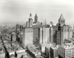 New York circa 1912. "Big buildings of Lower Manhattan." Landmarks here include the Singer Building and, under construction, the Woolworth tower. And let's not overlook the Hotel Grütli. Detroit Publishing Company. View full size.
SurvivorsMany buildings in this photo are still going strong.  Woolworth, Bankers Trust, 2 Rector St., 111 Broadway and, of course, Trinity Church.
What else I didn't know there was an elevated train on Trinity Place as well as Greenwich Street. Off in the distance is the Met Life Building, with no competition, and at the right the grand old Municipal Building is nearing completiion.
El of a PhotoThe two Tracks shown at the bottom photo are the 6th Avenue (on the right) and the 9th Avenue(on the left) Elevated Lines where they have just diverged from a common track above Battery place and the South Ferry terminal. The 9th Avenue El is also seen further uptown in the photo.
The photo also shows the NYC Municipal building under construction and way uptown, the Metropolitan Life building, shown in many images here.
Those buildingshold more people than the 25,000 from my town.
Coming soon to a Broadway block near youThis view would soon be transformed by the construction of the new Equitable Building at 120 Broadway, between Pine and Cedar Streets. The old Equitable Building burned down in a spectacular fire on January 9, 1912; the Chicago architecture firm of Graham, Burnham &amp; Co. designed its replacement, which was built between 1913 and 1915. Although it was hardly the tallest skyscraper in downtown Manhattan, the new Equitable was one of the bulkiest, and it was heavily criticized for blocking out the sun from the downtown streets. Shortly after it was completed, New York adopted the Zoning Ordinance of 1916, which placed limits on the height and bulk of tall buildings; this law promoted the "setback" massing that characterizes so many NYC buildings built after 1920. 
With apologies to the Beach BoysWith trains on either side of the building, rooms in the Hotel Grutli would have had good, good, good, good vibrations.
Tall, Taller, TallestWhat a great snapshot(!) in time. This image captures the progression of the tallest buildings in Manhattan from 1894 to 1912:
The 1894 Manhattan Life Insurance Building (black baroque topped building in front of Bankers Trust pyramid, after its 1904 expansion).
The twin-domed 1899 Park Row Building, just to the right of the Singer tower of 1908 (lantern-topped building with flag).
The Metropolitan Life tower of 1909 (in the distance, through the haze).
Finally, the Woolworth Building (under construction, completed 1913).
(The Gallery, DPC, NYC)