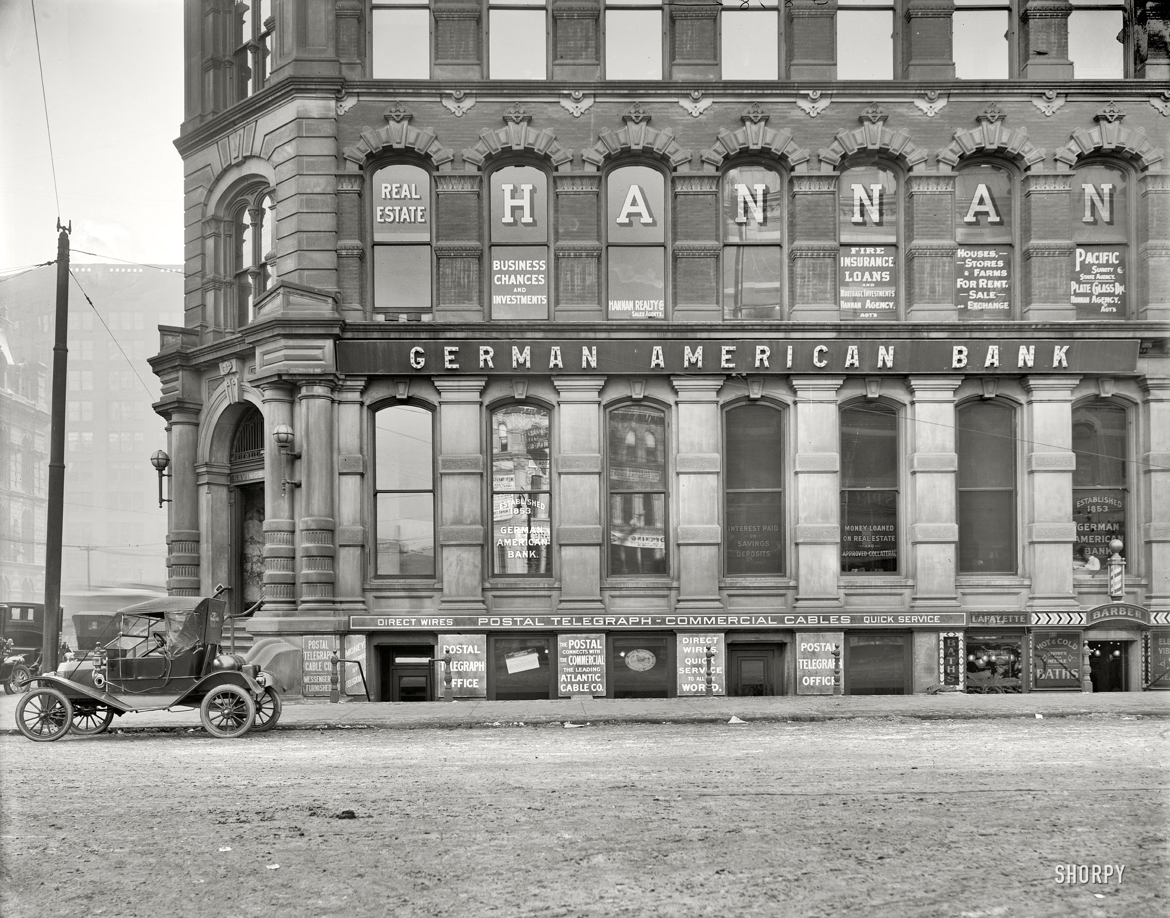 Circa 1911. "Postal Telegraph Cable office below German American Bank. Possibly Detroit, Michigan." Downstairs: Lafayette Barber, offering Shower and Needle Baths, and something to do with electric vibra[...]. View full size. For a closeup of the Model T, click here. For the rest of the building, see this post.