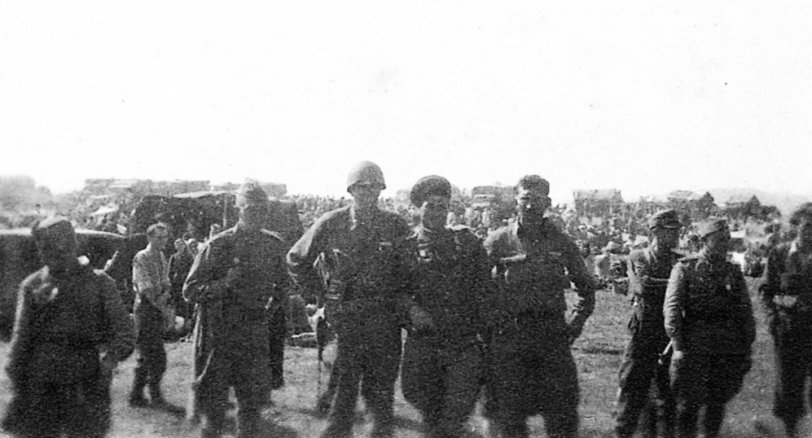 Cropped enlargement of an original print size 2 in. by 2 in. Inscription in fountain pen on back: "Get this enlarged.  Our Lt, a Russian major, and myself.  German PW camp in background." My uncle's unit was the 4th Armored Division, 51st Armored Infantry Battalion, Company A. No date.  Possible location Germany or Czechoslovakia.
