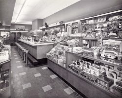 Early 1950s lunch counter somewhere in northern New Jersey that sold candy, cigars, small gifts and toys. View full size.
I remember hundreds of theseI grew up in Brooklyn.  I remember hundreds of stores like this. We had one on Kingston Avenue, in Crown Heights.  My grandmother would take me for "a malted."  One could, of course, get an Egg Cream, as well, which contains neither eggs nor cream. 
Note also the two wooden phone booths in the back and the older mechanical cash register behind the soda counter, in counterpoint to the electric cash register at the front counter. 
Some of the stuff for sale is interesting. Wind-up alarm clocks (top-right). Camera equipment -- Ansco something.  Brownie camera, Kodalite Flashholder.  A tricycle and a kids tractor up above the phone booths. 
Betcha they don't offer wi-fi.
LuncheonetteAlternate title: A Kid's Dream Come True. Toys, candy plus burgers and shakes all at your fingertips. These are great vintage store and pharmacy shots, obviously done by  commercial photographers. How did you come by them?
So many thank you&#039;s shorpy, this one is awesome!The candy store -- growing up, as a little kid in the fifties, let me be very clear, I was six years old, left my house to walk three blocks to the most incredible place on earth; the candy store! No parental supervision, just a total array of colors, sodas, newspapers, comic books and most of all, candy. We were poor so the only way to buy a piece of candy was to sweep some neighbor's yard or collect deposit bottles.
This brings it all back. I wouldn't trade being poor vs. rich for anything. I appreciated that five cent chocolate bar immensely.
Thanks Shorpy, you rock!
El ProductosGood to see that the store has a good supply of El Producto Cigars. You never can tell when George Burns might wander in looking for his favourite brand. Burns smoke 10 El Producto Queens a day for most of his long life. He'd order them in batches of 300 from the manufacturer and if his shipment was late he'd call the factory and send his butler out to get as many as he could find.
How I got my imagesOwning an antique mall has been one source for finding some of my images. Some of my vendors know what I look for and  show me before they put them out for sale.
Ebay has been a source obviously. I've been buying since 1997.
My third resource, and most prized, was from a former coin-op book author who passed away over 10 years ago. I bought several original images that he used in some of his books. I plan to upload some of those here.
Dessert under glassLove this with the Coke clock and soda machine. Twelve stool counter equals a busy soda jerk. The phone booths probably each have a fan that is automatic. Brings back some memories from childhood.
I want a hamburger and a real  Coke with cane sugarAfter I'm done I'll wander over and get a 10 cent Hershey Bar that's twice as big as the one you get today.
Counter servicejimmylee42, you're on the beam, but instead of a soda jerk I see a large middle-aged gal with bright red fingernails who calls you "Hon."
A trip downtownThis scene so reminds me of the shopping trips made to the SS Kresge, FW Woolworth , or the Metropolitan store in downtown Windsor Ontario. The SS Kresge store had wood floors, I can still hear them creak. Now, where's the toy department? Let's see the new Dinkys.
Vintage EatsSomething tells me this was either a Woolworth's Or McCrory's. Being from North Jersey I'd go with the latter.
Let There Be LightWhen you closed the door in the phone booth, the ceiling light would come on. A nickel had been the price for a local call for decades, but by the mid-1950s it had doubled to 10 cents in most places. It was a surprise to find that it was still 5 cents on a visit to New Orleans in 1976.
Delightful memoriesNot only do I want to buy those two riding toys for my granddaughters, but I want to have a leisurely lunch at the counter and scan the items for sale!!!
Misspent youth, of courseTakes me back to cherry cokes at the Peoples Drugstore at Fesseden and Wisconsin Ave., Friendship Heights, D.C. Boy, were they delicious!  Sigh!
The good old daysWhen you could pick out and buy one thing instead of a plastic-encased "multipack" with three or four of whatever you just needed just one of.
RepurposingI'm a big fan of antique shops, and can't recall how many shops I've been in (mainly in small towns) that were originally drug stores or something similar, with many of the original fixtures still intact (lunch counter, back mirror, wall displays, etc.).
And a lot of the items in this photo can still be found in those shops -- Coca-Cola clock, Ronson lighters, pedal cars, countertop display cases, alarm clocks, etc., albeit at much higher prices than in 1950.
Deja VuThough I never visted this lunch counter, when I saw this photo I felt I had been there before.  Growing up in the fifties, I ate at many a lunch counter that looked just like the one here.
AgogLook at the firetruck with the raised ladder, in the second overhead cubbyhole (visible in the mirror)!  I always wanted one of these but we could never afford one.
To the kids this must have been a fantasyland!
&quot;Hon&quot;tterrace, As  a former resident of northern New Jersey, I can almost guarantee you the "large middle-aged gal with bright red fingernails" would NEVER call you "Hon." 30 years ago I moved to Maryland, where the "Hon" is quite prevalent, and I remember being quite shocked when a total stranger addressed me that way.
My OrderI'll have a cup of coffee and a piece of that banana cream pie. How much will that be? Fifty cents? I don't want to buy the whole place, I just want a cup of coffee and a piece of pie. Next thing you know they're going to charge a quarter just for a cup of coffee.
1950 InventoryMissing in stores today:
Kodak and Ansco Film
Ronson Cigarette Lighters
Irvin S Cobb Corn Cob Pipes
Westclox &amp; Big Ben Alarm Clocks
Waterman Pens
Scripto Mechanical Pencils
Dills Pipe Tobacco
Blackstone, Robert Burns &amp; El Producto Cigars
3 in 1 Oil
Still There:
Tums
Kleenex
Topps Gum
Coca Cola
I was surprised to find outThat you could still buy one of those Moist-N-Aire machines.
I'd like to have a cherry Coke, club sandwich and an order of fries, please.
Complete blast from my past!My father owned a Luncheonette in Passaic until 1977. I have some fond and some not-so-fond memories of it.  But everything in this photo rings the nostalgia bell in me.
His store wider than this, but the stools and counter and various wares are all familiar friends.
My job at the age of 4 was to stock cigarettes and make Heinz soup in the electric soup maker. I still have two of his three malt mixers and they still work!
Thanks for the memories.
Are those bunnies?As I time-traveled back to 1950 to stroll around this wonderful establishment, I think it was near Easter because on the top of the display counter on the extreme left there appears to be a display of cellophane-wrapped chocolate rabbits near a collection of chocolate eggs in egg cartons.  Also, on the far back wall, left side of photo, it looks like Easter candy novelties.  Of course it could just be wishful thinking since there was something unique and especially delicious about chocolate rabbits in those days that just do not taste the same anymore.  
RonsonsI see my dad's old lighter on display. All that's missing is the pack of Parliaments. Having grown up in NYC this brings back such fond memories.
A couple of things that haven&#039;t changed.Note the napkin the sugar dispensers. Go into any Waffle House in the South and you will find those exact dispensers. I always hated the napkins, they were too small and light.  Couldn't clean your hands if you got syrup on them.
But I love the photo, brings memories of the great "real" milkshakes you could get at a drugstore counter. Made in a metal tumbler and poured into a real glass. The chocolate was great not the imitation you get nowadays.
And of course the paper straws.
Thanks for sharing.
Give or take a year or twoMost Europeans were just getting rid of ration cards. So a store like this would have been a major cultural shock for them, even for those who had actually been off rationing for some time.
West of the Iron Curtain, that is. East of that? I can't even imagine. 
I&#039;d be sitting at that counter!Wow, does this photo bring back memories. It looks just like the place my friends and I would "hang out" at at lunch time and after school, right down to the way it's set up with the phone booths in back.  We'd buy cigarettes from a machine (put in 30 cents and get 2 cents change back on the side of the pack). Luckily, I didn't smoke too long. Cokes were either 5 or 10 cents and an order of fries was 15 cents. The guy who owned the place and his wife were like grandparents to us. They really cared about the kids.
Pens and phonesYou can still buy Waterman fountain pens, Mr Mel ... but not in a drugstore.
But when I looked at this photo, I tried to imagine getting to the phone booths past a couple of kids spinning like dervishes on those stools.
(ShorpyBlog, Member Gallery)