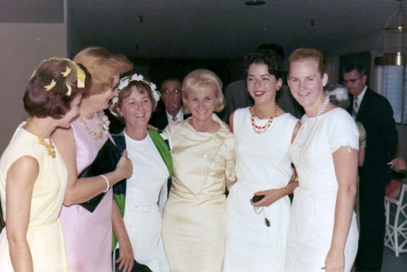 The wedding party. St Petersburg, Florida, April 23, 1964 at Temple Beth-El, Pasadena Avenue South.
My parents' wedding day. My mom is at center in the off-white dress. These are her bridesmaids and friends. The matron of honor is second from left in the pink dress. Her name was Wilda; she was also a hairstylist and did my mom's hair for the wedding. 
I love the profusion of pearl necklaces, netted hats and silky sheath dresses. Fashion was great back then. Very "Mad Men"! 
My parents were married for 37 years.
