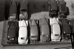 May 1940. Parked cars in Des Moines, Iowa. View full size. 35mm nitrate negative by John Vachon for the Farm Security Administration.
ZORThe Mark of Zorro w/ Tyrone Power came out in 1940, but it wasn't released until November.
Besides, I would expect a slashing Z rather than the boxy typeface they used here. And, of course, no apparent room for 'The Mark of'....
Isn't the Internet a wondrous thing?
And for all you film buffs out there, there is some extant gag footage (there's a phrase you don't hear every day) of Ty Power doing his trademark Z, but it's referred to on the soundtrack as 'gasp', the Mark of Zanuck! 
but, I digress....
Reading MaterialIn the white car second from the left, looks like there's a newspaper in the back. Wonder what the headline was.
[ZOR - Dave]

ParkedI wonder how the driver got out of the cars after he parked them, or how is he planning to get in. Maybe they put first the car on the right, then the next one to his left and so on. Kind of a Tetris game!
SpaceIt looks like they still had about 1meter of space to open the door and go. But the way they were planning to get out of this parking must be interesting.
On the other hand it looks like a parking for office or small factory workers, so probably, as they ended work at the same hour, there was no problems with driving away.
[I think this was the view from John Vachon's hotel window. - Dave]
Running BoardsAll these cars have running boards, which means that although tightly packed, a driver could step on the adjoining car's running board as he got into his own car. It is odd that they would be parked so closely, though.
[These would have been parked by an attendant, not the owner. - Dave]
Bumper CarsA couple of these are brand-new cars.  The second from the left in upper row with the one chevron-shaped taillight is a 1940 Ford standard coupe (the Deluxe had two taillights). Apparently in those days the bumper was there to bump. They must have backed the cars up 'till they heard or felt contact.
Parking lot?I read all the theories about the parking methods used in this "parking lot", but I think it more likely to be the parking lot of a car seller. That is the place where you, also nowadays, will find cars parked like "herrings in a barrel" (like is said in Dutch).
[You don't leave hats and packages in cars for sale. It's a typical urban pay lot, familiar to anyone who lives next to a vacant patch of land in a big-city American downtown. They still park them like this today. - Dave]
Washington D.C. parkingI worked in Washington during the early 70's and commuted to work in my personal car.  The parking lot was behind the Old Post Office off of Pennsylvania Avenue. The attendants would start in the center and pack the other cars around it until the lot was filled. You can imagine what would happen if a person wanted to leave work early!
(The Gallery, Cars, Trucks, Buses, John Vachon)