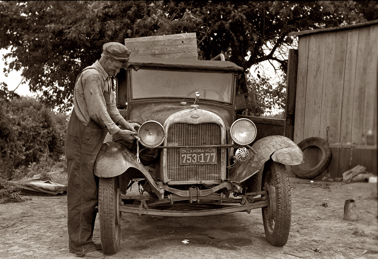 July 1939. "Elmer Thomas, migrant to California, tying sack of laundry onto front lamp bracket near Muskogee, Oklahoma." View full size. 35mm nitrate negative by Russell Lee, Farm Security Administration.