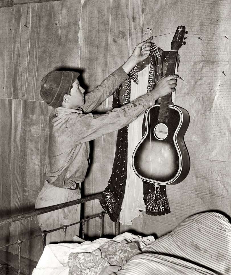 July 1939. "Migrant boy removing guitar before family leaves for California. At old homestead near Muskogee, Oklahoma." View full size. Medium format safety negative by Russell Lee for the Farm Security Administration.