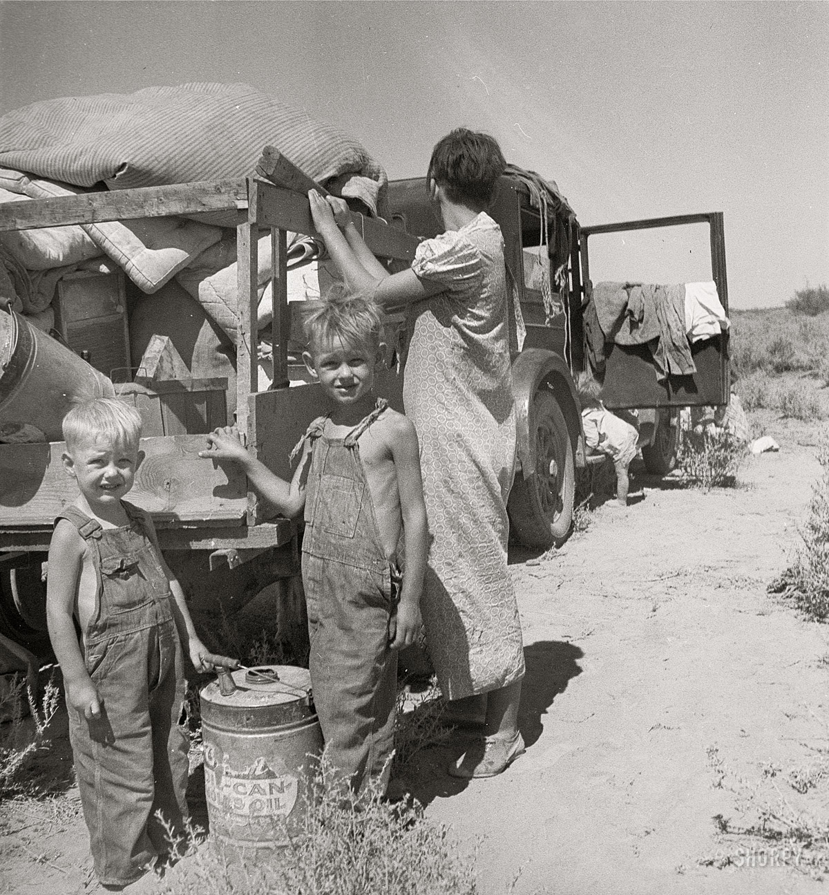August 1936. "Part of an impoverished family of nine on a New Mexico highway. Depression refugees from Iowa. Left Iowa in 1932 because of father's ill health. Father an auto mechanic laborer, painter by trade, tubercular. Family has been on relief in Arizona but refused entry on relief rolls in Iowa to which state they wish to return. Nine children including a sick four-month-old baby. No money at all. About to sell their belongings and trailer for money to buy food. 'We don't want to go where we'll be a nuisance to anybody.'" Medium-format nitrate negative by Dorothea Lange for the Resettlement Administration. View full size.  