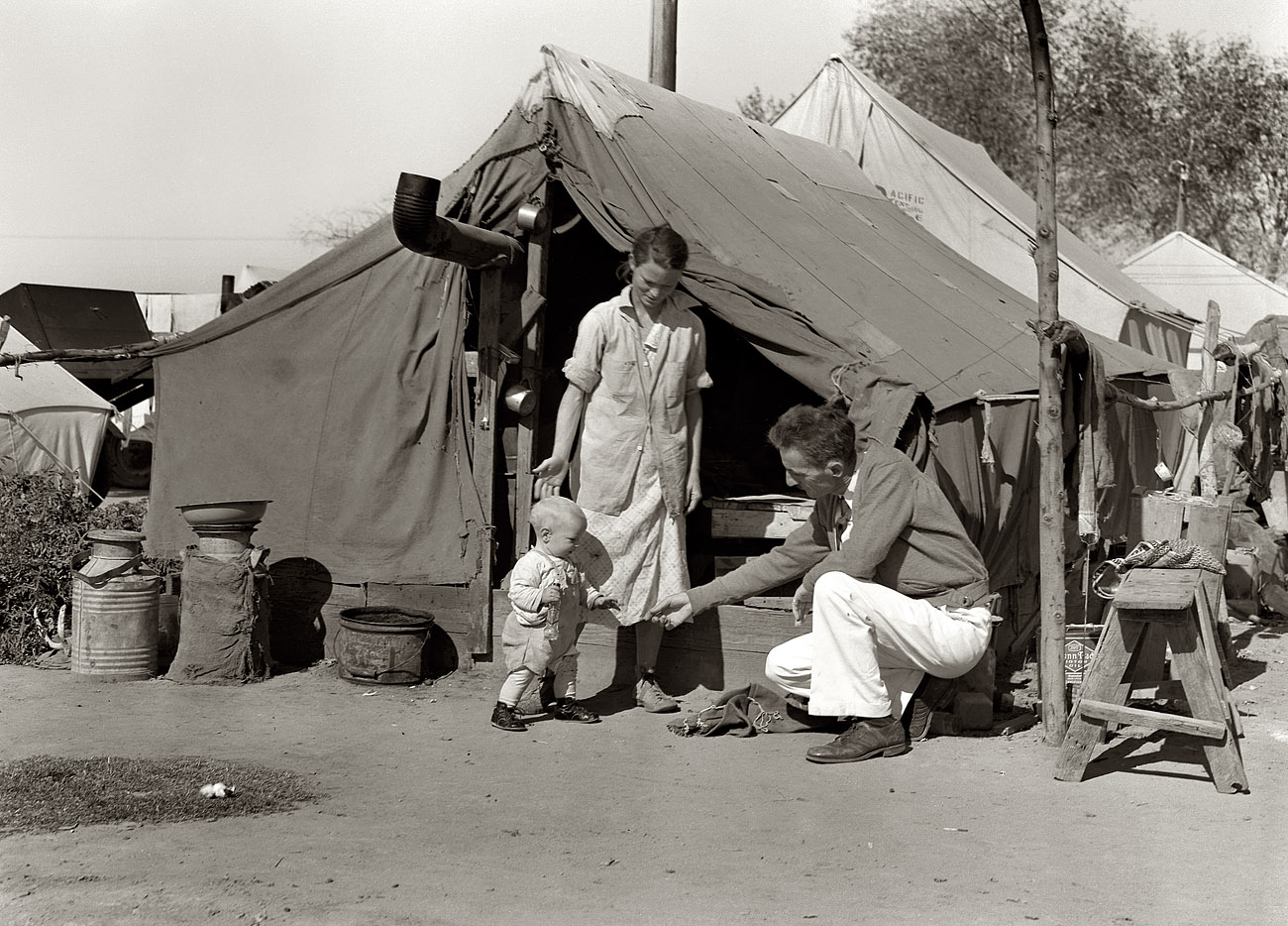 November 1936. Arvin migratory farm workers' camp in Kern County, California. "Tom Collins, manager of Kern migrant camp, with drought refugee family."  Medium-format nitrate negative by Dorothea Lange. View full size.