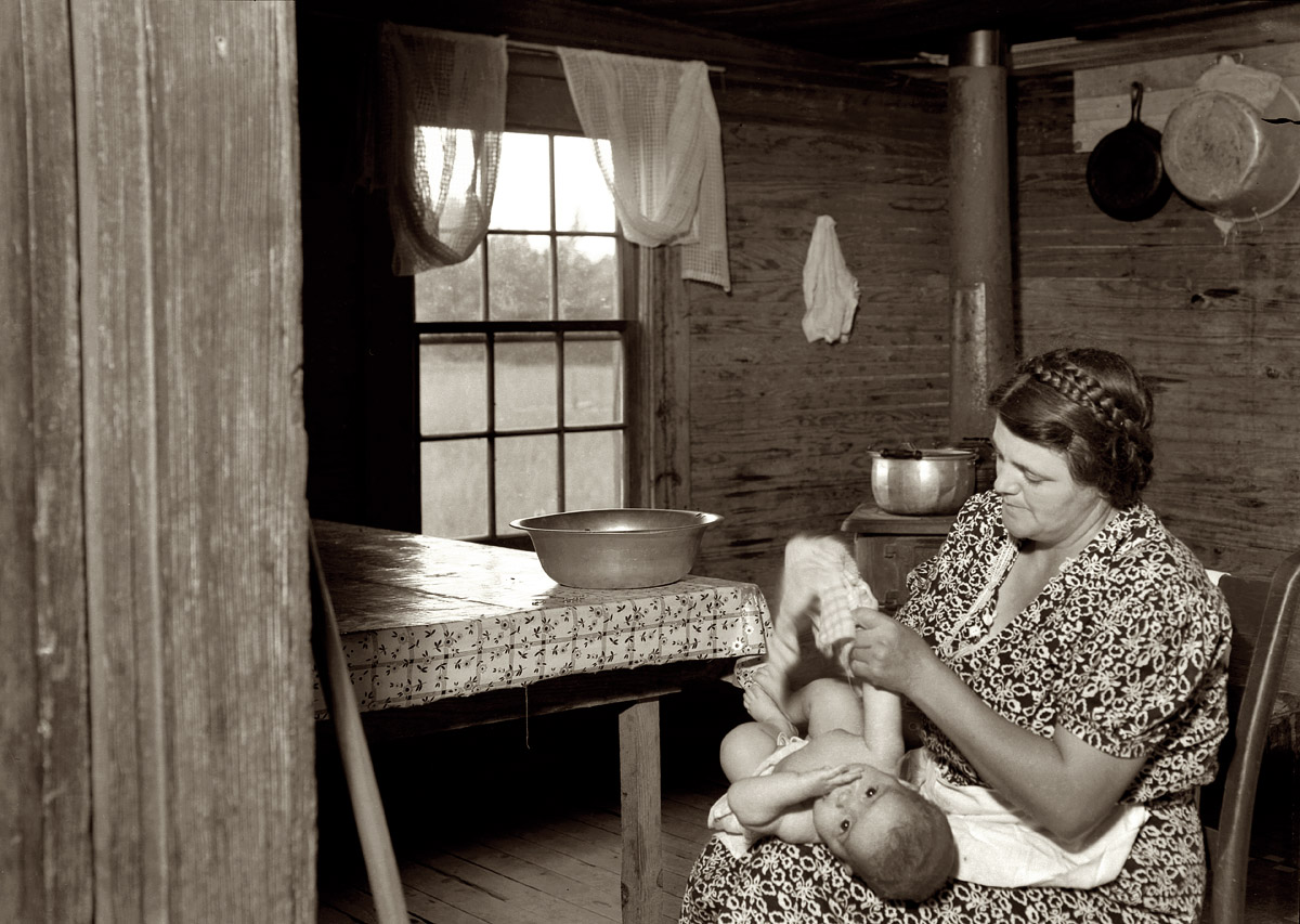 July 1939. Whitfield family. Wife of tobacco sharecropper drying the baby after its bath in the kitchen. Person County, North Carolina, near Gordonton. Medium-format nitrate negative by Dorothea Lange for the FSA. View full size.