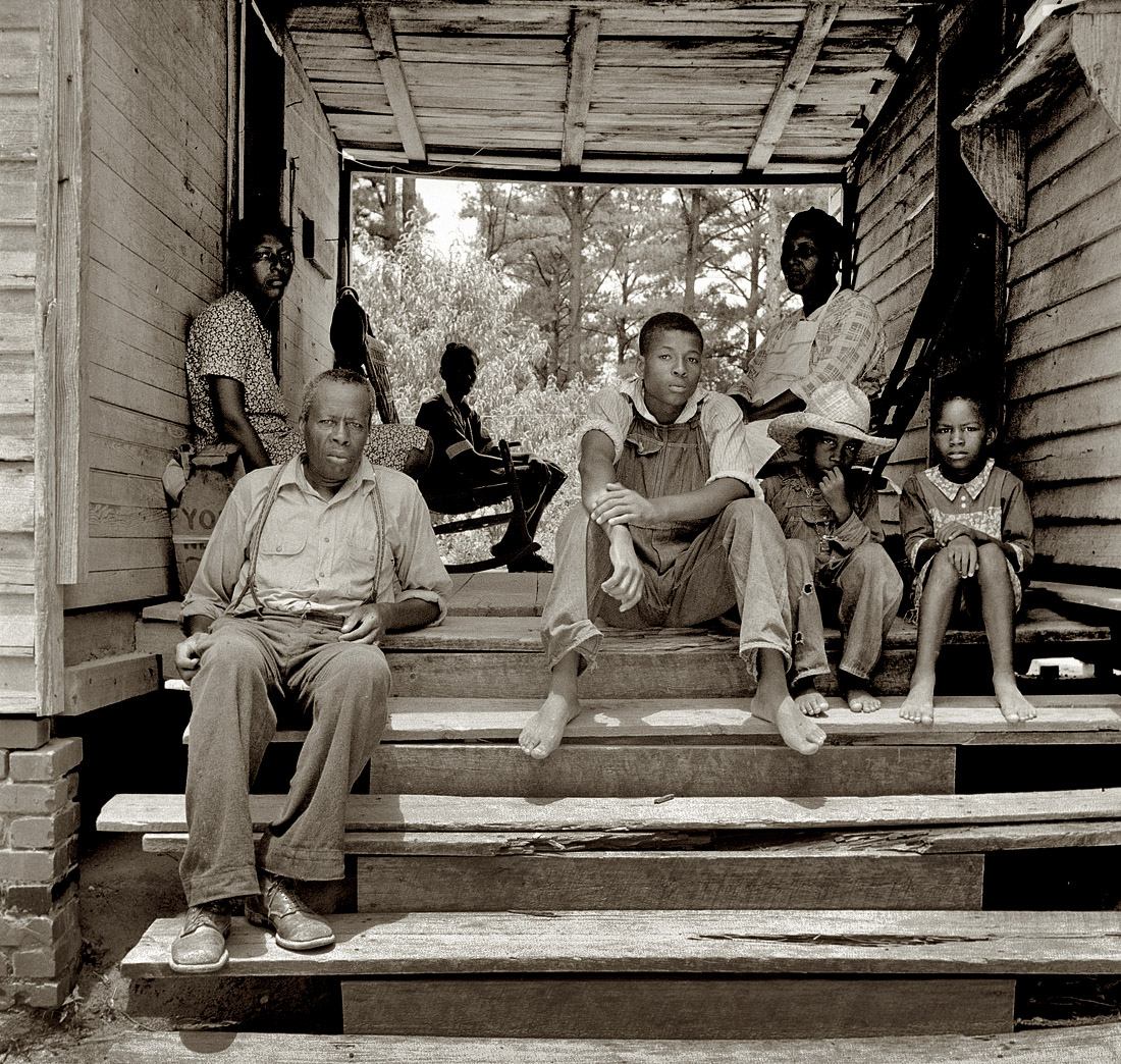 July 1939. "Zollie Lyons, Negro sharecropper, home from the field for dinner at noontime, with his wife and part of his family. Note dog run. Wake County, North Carolina."  View full size. Medium-format nitrate negative by Dorothea Lange.