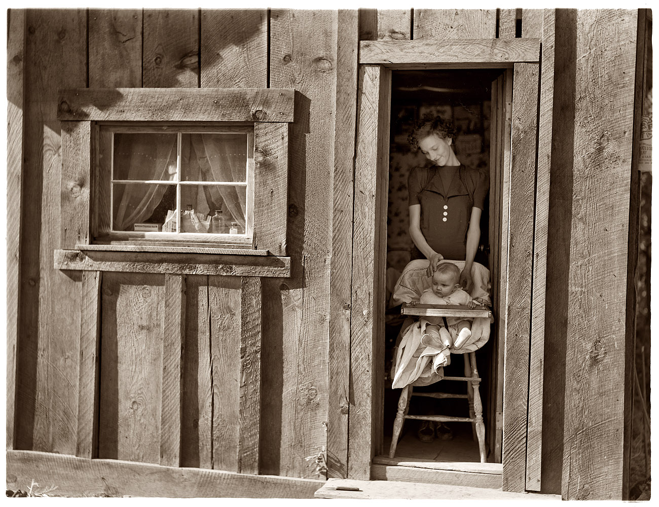 October 1939. Wife and baby of of the Ola self-help sawmill co-op president in the doorway of their home. Gem County, Idaho. View full size. Scanned from a 4x5 inch nitrate negative photographed by Dorothea Lange.