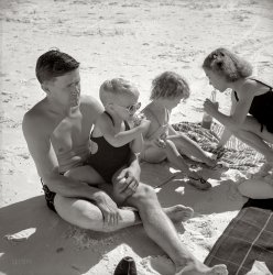 January 1941. Sarasota, Florida. "Guest of Sarasota trailer park with his family, picnicking at the beach." Photograph by Marion Post Wolcott. View full size.
Sands of TimeThe little girl holding the soft drink would now be in her mid-70s.
Re: Sands of TimeWhen this picture was taken, I was four and also sat on my father's lap at the beach (though in the summer in the Northeast) in the company of my two older sisters.  Only I and the youngest girl survive.
MaturityIt may just be current-generational predjudice, but photos of that era and earlier reveal an earlier maturity for the adults of the time.  The dad in the photo can't be more than 35, but compare his photo to men of his age today.  Advanced juveniles; and our society seems to show it.
Back thenthe farthest my family could travel to the beach was to the Irish Riviera, a.k.a. Rockaway Beach, Queens.
FinallyThe first appearance of beach blankets on Shorpy!
Suits HimI have a photo of my dad in the early 30's, about that boy's age, wearing the same kind of bathing suit.  Always seemed like a weird style to me.  
Maturity 2Well, the dad in the photo just spent the prime days of youth (late teens to early twenties) in the Great Depression.  His thoughtful, distant gaze is no doubt imagining World War II raging across the ocean his family is frolicking beside.
[The often-overlooked Mexican Campaign? - Dave]
Earliest known photoOf Sir Elton John!
(The Gallery, Florida, M.P. Wolcott, Travel & Vacation)