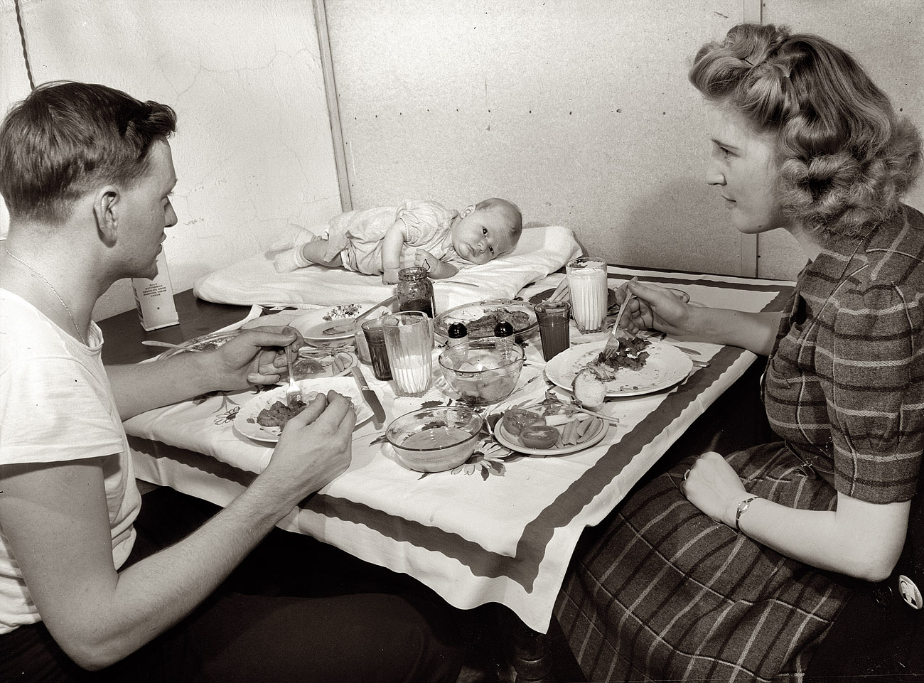 December 1943. Washington, D.C. "Hugh Massman, a second class petty officer studying in Washington, and his wife eating dinner. Joey, their son, sleeps on a pad on the table." Medium-format negative by Esther Bubley. View full size.