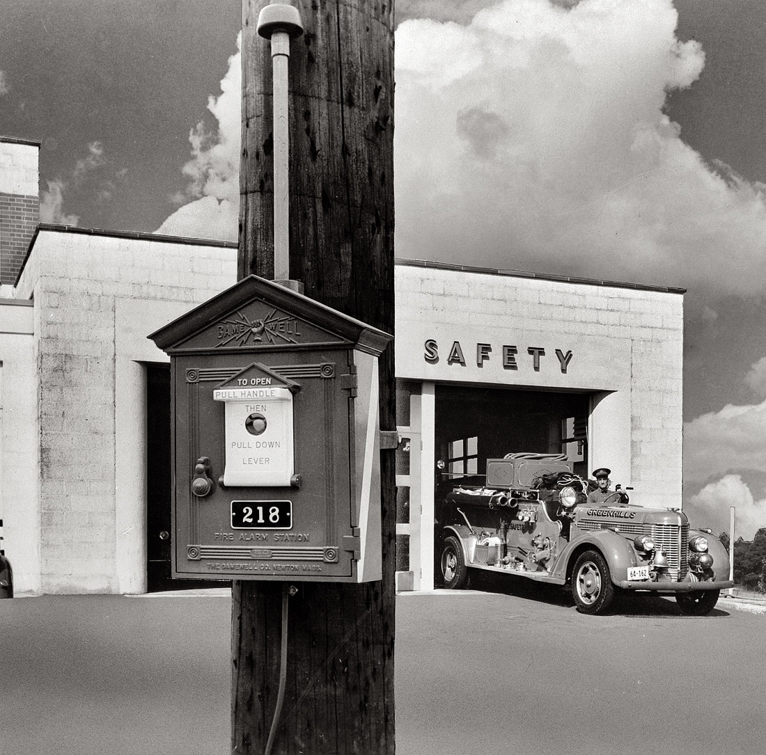 October 1938. Fire station at Greenhills, Ohio, a planned community built by the federal government (Suburban Division of the Resettlement Administration) during the Depression. The image, scanned from a print, is a composite, with the utility pole and fire alarm superimposed; the asphalt was retouched with an airbrush. View full size. The fire station photo is by John Vachon.