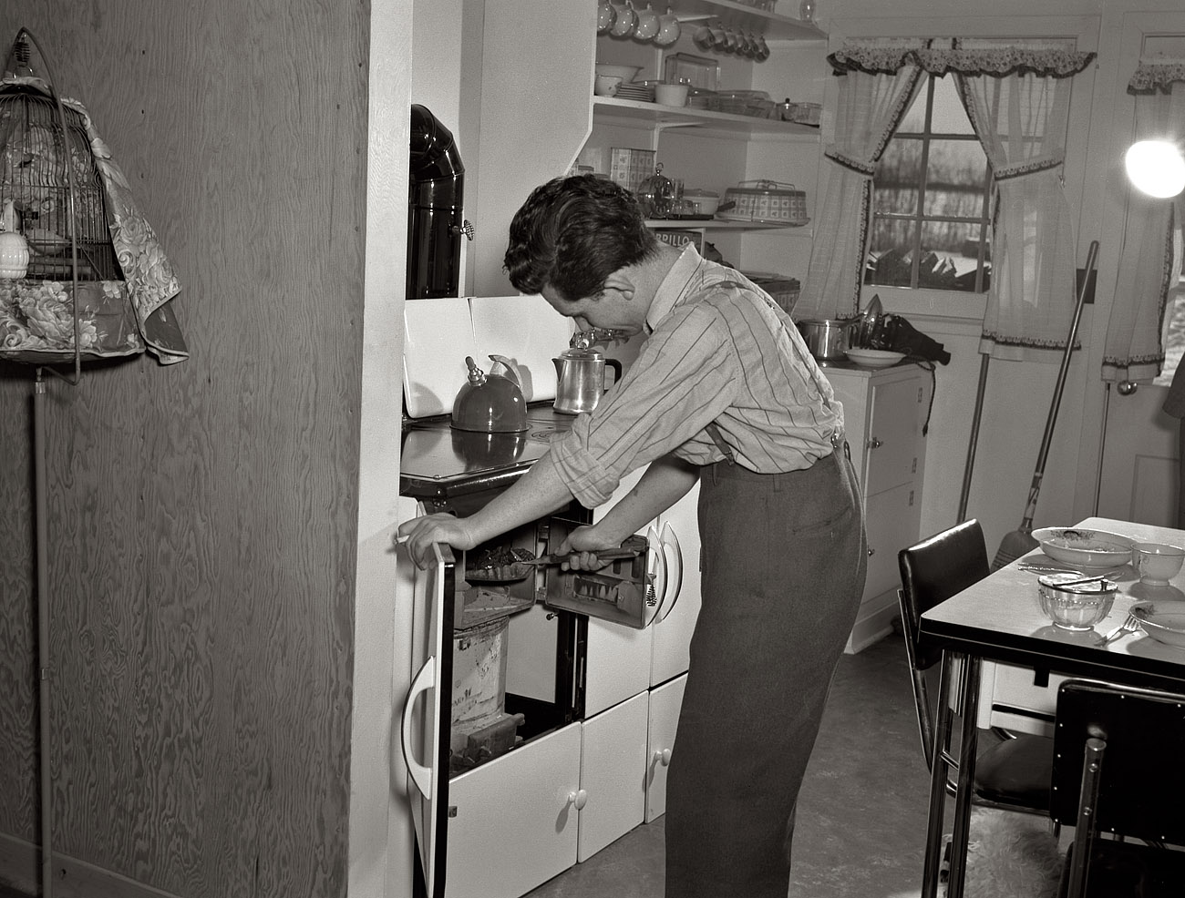 January 1942. Bantam, Connecticut. "Defense homes. The heating unit is in the kitchen of Fred Heath's four-room apartment in the new federally-financed homes for 80 families just a few minutes from the Warren McArthur factory in Bantam. The well-insulated coal fire puts steam in the radiators and provides the heat for cooking. The tenants are well-pleased although on several nights when the temperature dropped to 10 degrees below zero they were forced to replenish the fuel every two or three hours. That cigarette Fred Heath holds is not tailor-made, by the way -- he likes to roll his own." View full size. Medium-format nitrate negative by Howard Hollem for the Office for Emergency Management.

