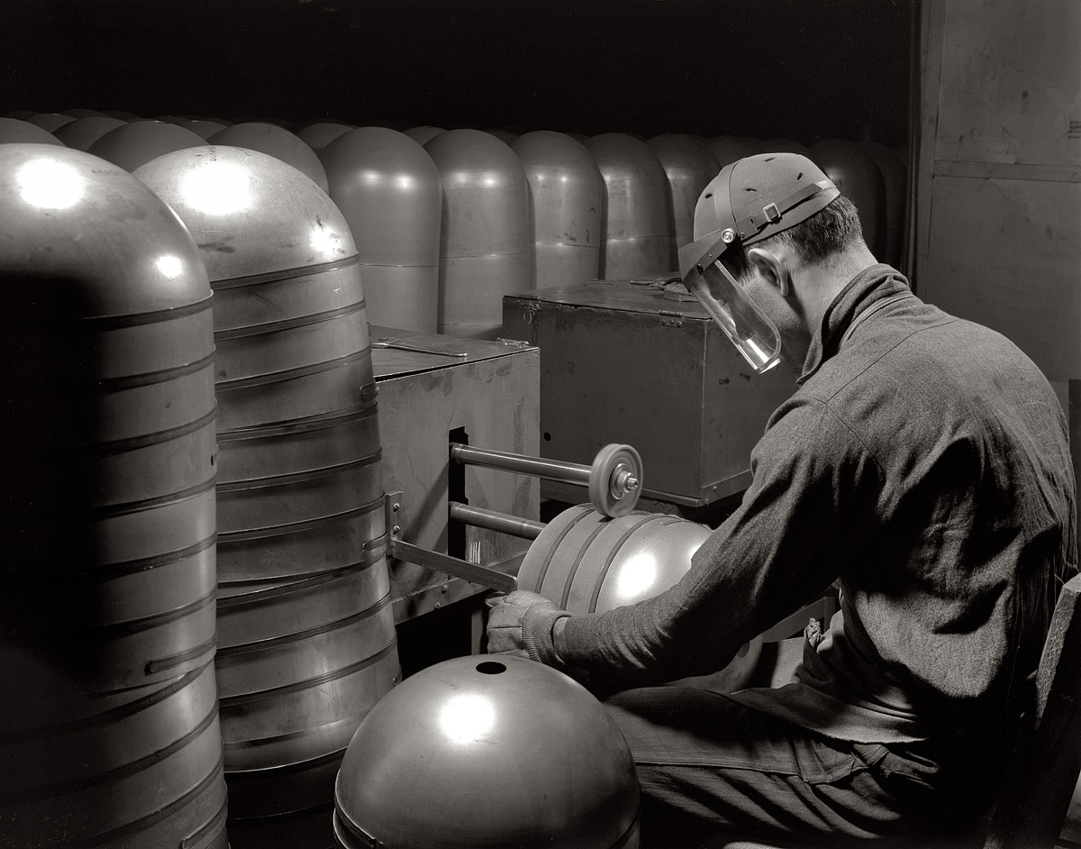 Firestone rubber plant. Akron, Ohio. February 1942. "Conversion. Beverage containers to aviation oxygen cylinders. After the circumferential straps are welded to the cylindrical portion in the metal division of a large Eastern rubber factory, rough edges and accumulated weld scale are removed by a skilled workman. The twin rotary brushes do their work on the inside and outside of the cylinder in the same operation. This process is required in the manufacture of shatterproof oxygen cylinders for high altitude flying." 4x5 nitrate negative by Alfred Palmer for the Office of War Information. View full size.