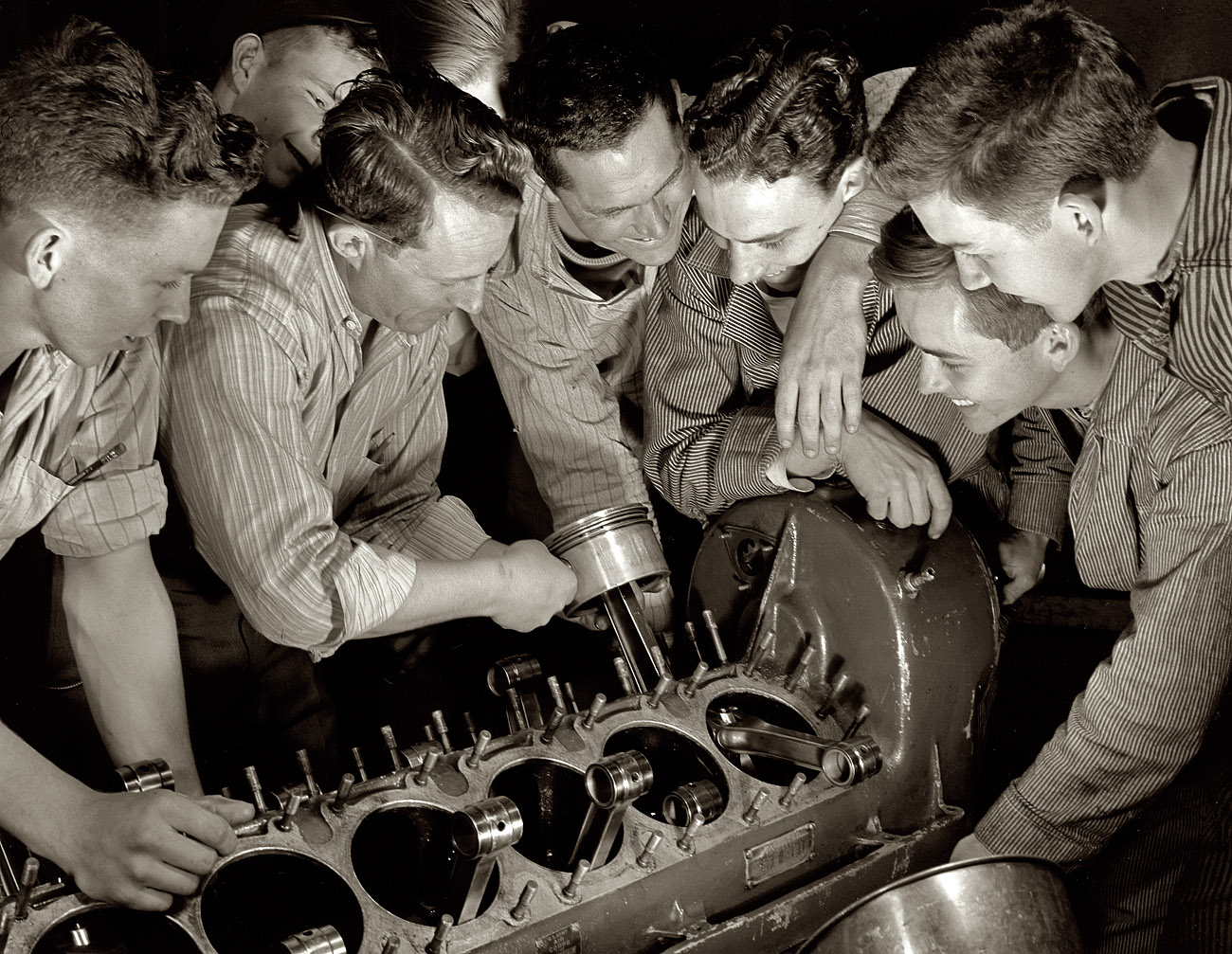 April 1942. De Land, Florida, machine shop pool. "Aircraft construction class. These carefree high school students are learning the serious business of war production in a Daytona Beach vocational school located in a revamped nightclub. Instructor Gil Angell (with piston in his hand) is showing the group how to assemble an airplane engine. Left to right are Wilson Flippo, Angell, Dewey Stewart, 19; Ken Kirkpatrick, 18; Bill Jackson and Ned Brown, 18. Jobs already are waiting for most of them when they finish their courses." View full size. Medium format safety negative by Howard Hollem for the Office of War Information.