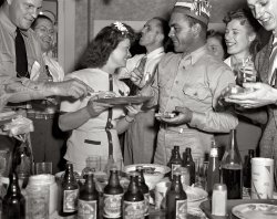 August 1942. "A poster comes to life. Another democratic institution, beer and pretzels. Chief radioman Evans, at extreme left, reaches for a slice of the ham which Mrs. Woolslayer is serving. Sergeant Vineyard is wearing the paper hat. Allegheny Steel, Pittsburgh." One in a series of dozens of photos taken of the three men in a WW2 poster after they decided to get together. View full size. Medium format negative by Alfred Palmer for the Office of War Information.