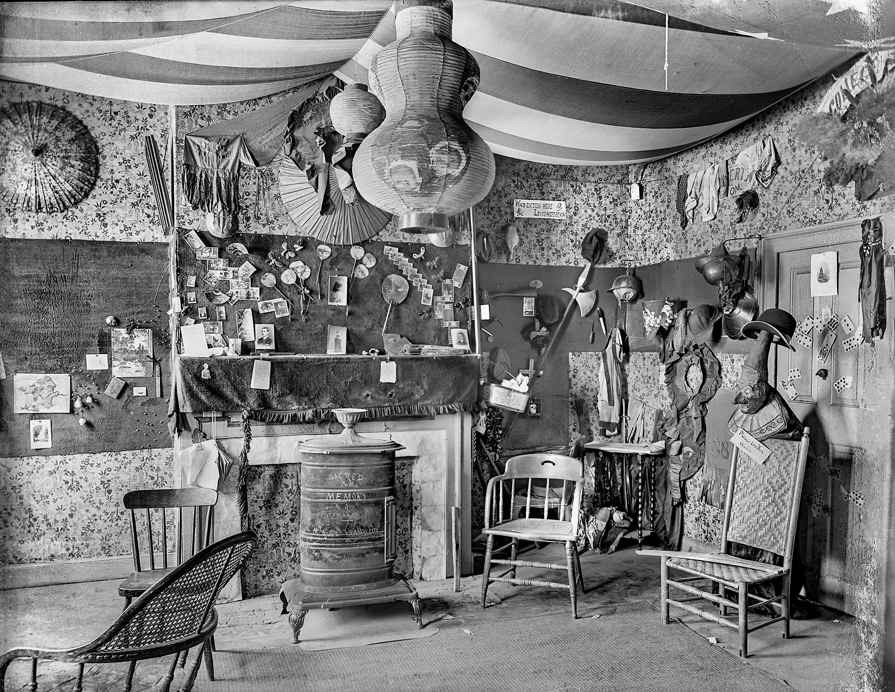 This room from well over a hundred years ago in Pawnee City, Nebraska, looks to have been the personal space of a boy or teenager. It's filled with weird little items a teenage boy might have found worth collecting. A handwritten sign on the wall says "WHO ENTERS HERE - LEAVE HOPE BEHIND". A large Punch and Judy puppet is mounted on a chair with a warning not to handle it. Playing cards decorate the walls. The scrawled message on the heating stove says "Sacred to the Memory of a Fireman - He has gone to his last fire". An American flag covers the ceiling. Browse around the room and see what you can find. It's his own private museum, the Voynich Manuscript of Victorian living space! Scanned from a 4x5 glass negative. View full size.