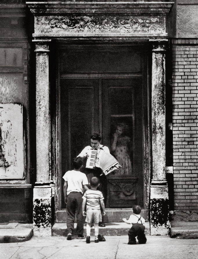 Taken in the Brownsville section of Brooklyn in 1959, on New Lots Avenue. This young fellow would come down to the street with his accordion and start to play. Invariably he would draw a number of children to his street concert. His mother would look on approvingly from behind the door. View full size.