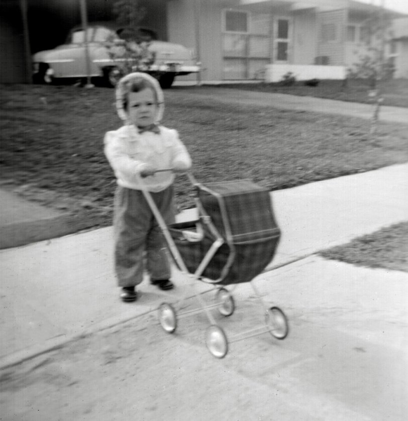 Another view of the great baby boom suburb of Levittown, Pennsylvania, in this case only three years after it was built. In it you can see one of the original mid-century modern homes, with its floor to ceiling windows and open carport. Best of all their mid-century Chevrolet is parked in it. I am the toddler with the stroller, playing on the sidewalk. My mother took the picture. I scanned it from a 2 inch by 2 inch negative.
