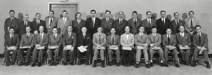 My father’s world was one of men in business suits back in a time when classified job ads specified if they wanted a man or a woman. If they said man, a woman could not apply. This group, who are holding certificates of some sort in their laps, seems to be the unsmiling graduates of something. Exactly what, I have no way to find out.
My father has hand-written all of their names on the back of the photo but I will bet you can spot him without me telling you where he is. My father is the one and only guy in this picture sporting a bow tie. View full size.
