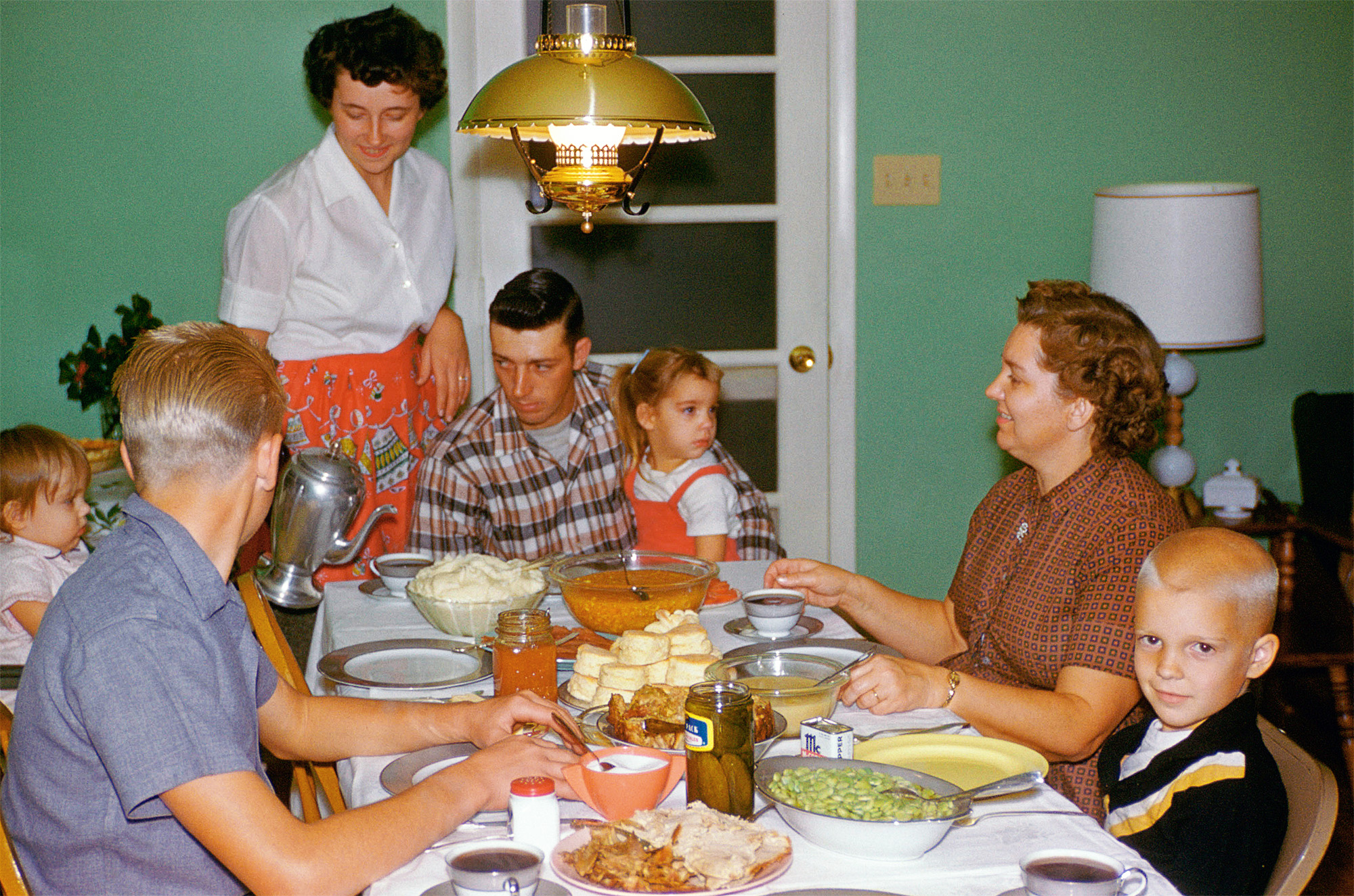 Family dinner just beginning. The color scheme in this photo just tickles me to no end. That green and the vibrant orange. Plus that meal sure looks good. The biscuits are made using an old family recipe and I can confirm that they are as good as they look here. Woodrow's Kodachrome slide. View full size.