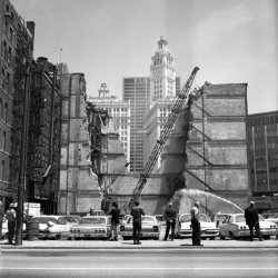 Chicago, Il, 1960's-ish. This is one of the 30-40,000 6x6 negatives discovered at a local auction here in Chicago by a photographer named Vivian Maier. View full size.
Welcome to Shorpy!I've read about your discovery of her cache of negatives. It's a fabulous body of work, all the more amazing that she made such strong, well-composed photos without the visual feedback of even bothering to develop most of the film! 
And it's more astounding that the film withstood the years and allowed such good results when it was finally processed. 
Thank you for rescuing these photos. Thank you for sharing them. Vivian Maier's photos.
This is not Lilliput......but the guy on the right seems to be playing Gulliver.
Chicago Sun Times to the rightI believe that's the Wrigley building behind and the Chicago Sun Times building immediately to (and mostly out of the frame) to the right, putting this on... Wabash?
Narrowing the date down a bit...The picture was taken in late '64 at the earliest - the right-most car is a 1965 Chevy Bel Air or Biscayne (the Impala had three tail lights). I learned to drive on a car just like that one.  
FordThat's a 1965 Galaxie in the middle.
(ShorpyBlog, Member Gallery)
