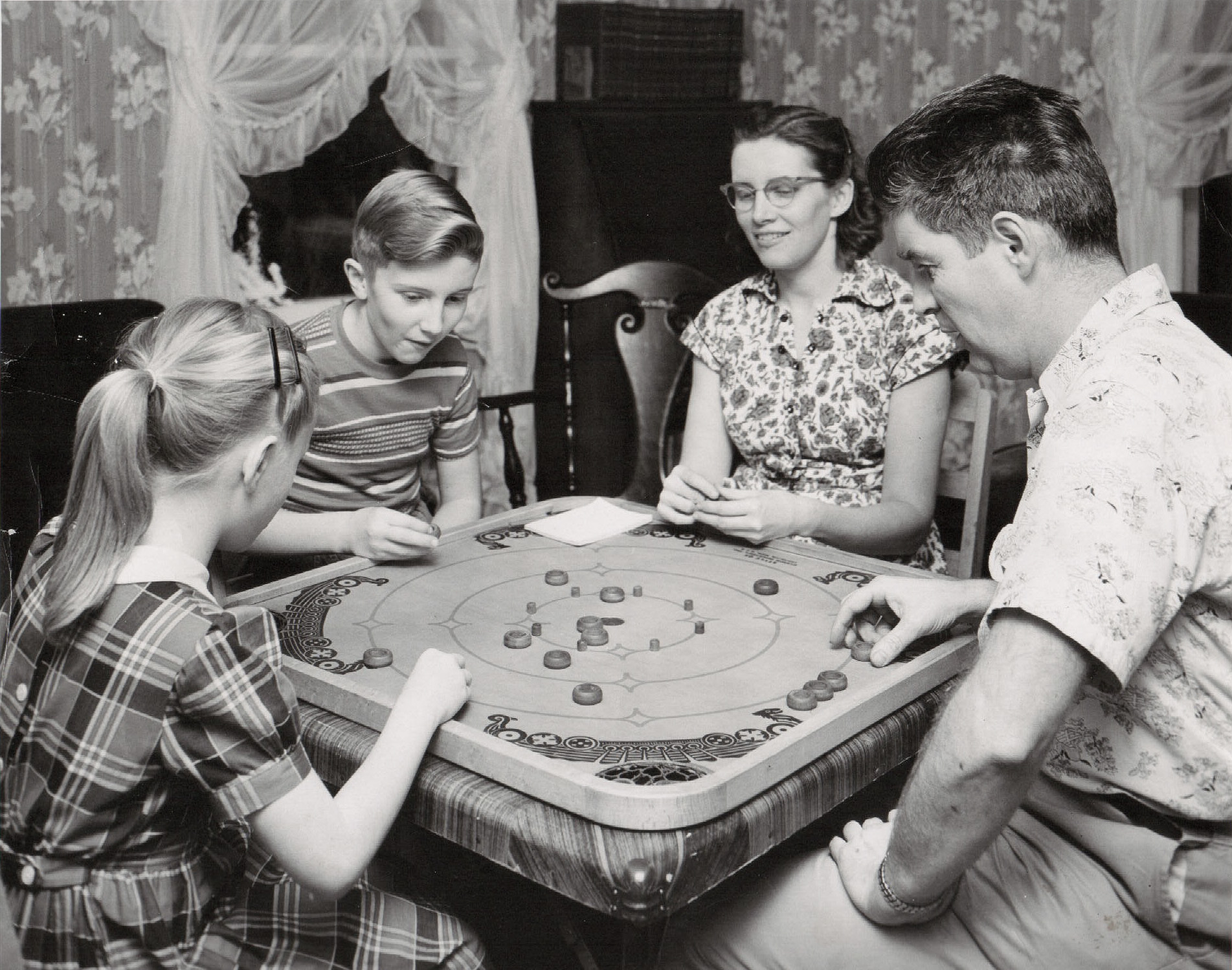 There was a time when people stayed at home and played board games with their family. This photo is from the archives of The Carrom Company that made this game, known as the "Carrom Game Board" or just "Carroms". Many versions of this game were made over the last 100 years in the Ludington, MI, factory, which is still in business. 

This is a Model K board made between 1939-1941. A rulebook that came with all the boards was filled with dozens of different games that could be played on both sides of the board. 

This photo was used for promotional purposes and I would guess it is from the mid to late 1940s. (My family owns The Carrom Company today.) View full size.