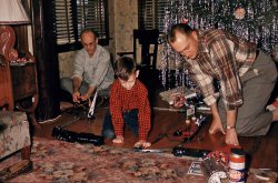 Christmas 1953. Oak Park, Illinois. My cousin Tom experiencing the thrill of his first Lionel electric train. My Uncle Bill is manning the transformer, and my dad, who was a real-life railroad engineer, is on the right. 35mm slide. View full size.
There&#039;s a tree somewhereUnder all that tinsel!
SparksWow! I can practically smell the ozone. This could have been me, except we didn't have sense enough to take pictures of anybody with our electric train, only pictures of it, like this one from December 1954. I think it's Lionel, I forget.

This was the time of my life.I might as well be in this picture. The timeline and all that is going on is perfect. Wonderful family shot. WOW! what great memories. Thank you and Merry Christmas to you and your family.
Tinsel HazardsHere's a question for you Boomers -- I see that tinsel was big in your growing up years (understatement).  Did people keep their pets outside then, or did they all just die horrible, tinsel-blockage induced deaths?  (I know that it doesn't always cause serious problems for them -- but with the sheer amount of tinsel on these trees, it seems like the chances for intestinal problems would be good.)
tterrace, I really like the attractively arranged couch pillows behind your train.  What were you hiding back there?  Or are they simulated mountains?
Who&#039;s having the most funI was so glad when our son was old enough (1957)for me to buy the thing I'd always wanted for Christmas but, because I was a girl, never got. Unfortunately, he was still at the push-toy stage so it didn't work for him but I had a ball.
Re: Tinsel hazardsWhy would pets be eating tinsel in the first place? None of ours ever touched the stuff. I grew up in the tinsel-lovin' Fifties. Dogs and cats eating tinsel was not anything people ever talked about happening. Sounds like some sort of 21st century consumer worrywart issue.
TinselitisI don't know ... because it's shiny and stringy and fun to play with?  My cat would go crazy for the stuff, as would most cats I've owned. Maybe even the pets were perfect in the 50s. It was just a question.
[It was an excellent tinsel question. Speaking of which: Garlands or icicles? We were always a garland family. Not that there's anything wrong with icicles. - Dave]
Simulated mountainsVery good, Catherine. I usually have to explain to people what the pillows are doing behind my toys in a number of my photos from back then. These we had retained from our old chesterfield which had been relegated to a slow, moldering death in the basement a couple years back. If you could look above them, you'd see my mother's renowned curtains and drapes.
We never used tinsel ourselves, but I remember enjoying it when we'd visit friends or relatives who did. Those were the days when tinsel was made of, or mostly of, lead. I liked to slip strands off and ball them up into little wads or, better yet, if there were lighted candles around and nobody was watching, dangle them in the flame and watch them melt. Don't tell anybody.
Twin tops?It appears that someone improvised and used some of the TinkerToy pieces to make stands for the 'billboard' signs. 
It also looks like the Tinkertoy was also a present that may have been wrapped in aluminum foil. And, there appear to be two identical toys in the picture, possibly spinning tops. 
Great picture!
TransformerLooks like the transformer is a Lionel model 1033 (made from 1948-'56). I have one of these units, still in perfect working condition. As far as I know, the only maintenance it ever had was the replacement of the power cord, due to the insulation drying out and cracking (a common problem). I never cease to be amazed at how durable those old Lionels are. Great picture!
LionelI agree, it's probably a Lionel in tterrace's photo. I had an American Flyer I received for Christmas in 1948. American Flyer did not have the middle rail in the track.
A way of lifeAs they say, a way of life gone with the wind. 
I love this blog . . .It is threads like this that keep me hooked on this blog.  It's comforting to know I'm not the only whack job walking around unattended.
Foy
Las Vegas
Cat TinselWithout the prompting of previous posters I wouldn't have mentioned that during the Christmas season at our house our Siamese cat Tabetha would walk around with a piece of what she usually left in her litter box instead dangling from a piece of tinsel she had once presumably eaten.  That's the most tasteful way I can explain it.
Now That&#039;s Christmas!Real Tinker Toys, the "real" old-school Lionel train sets, and not those modern knockoffs made by a company that simply owns the name. What do kids get today? Lead lined Chinese plastic "toys" from Wal-Mart.
Boy, give me that old fashioned Christmas anytime.
Thanks, and Merry Christmas to you. My Dad and Uncle have passed on, but Tom - who's now in his sixties - still has that Lionel train set. Last time I was at his house he had it set up in his basement, along with several accessories he's accumulated over the years.
[We're all glad he finally got to play with it! And thanks for this wonderful photo. - Dave]
Chestnuts roasting on an open plasmaThis picture just radiates warmth and good cheer. We're leaving it up all night on our plasma display. It's better than a fireplace!
California TinselI have to think our state banned tinsel production due to environmental concerns, because it's virtually nowhere to be found.
I say "virtually," because Michael's has it. No tinsel at the dollar stores and such.  At Michael's it is in packages that need to be cut. The tinsel comes attached at the top.  Same stuff.
Thanks to Michael's, our tree looks like this one.
[I think its scarcity might be due more to child-safety concerns. - Dave]
Nothing to add.I have nothing to add. Just love this picture and reading all your comments -- the wallpaper is killer. Shorpy forever.
How we tinseledAround our house, we would always begin with laboriously stringing one strand of tinsel at a time on a barren branch until it was somewhat filled. Yet invariably, we two boys would get rambunctious and throw a handful up where we couldn't reach. And Mom, patient Mom, would sigh and give us permission to begin the fusillade of tinsel throwing that produced a Christmas tree neatly stranded with tinsel about 3 feet up, but above that utter disorder that only little boys could love. But I hasten to add the "tidy line" rose as we grew. Making a much happier mom.
The Train Don&#039;t Stop Here No MoreMy Dad had a huge 60's-70's Lionel train set, with all the accessories: the lighted passenger cars, the little signal box with the trainman who would come out, holding his lantern when a train went by, and even the Giraffe Car. Anyone remember the Giraffe Car?
Several locos too, both steam and diesel, and that big control transformer with the power supply handles on both ends. The whole setup ran on a plywood table, about 6 x 8, which he built himself. Sadly, when he died, my mother sold the whole outfit for a hundred bucks, and today it would probably be worth ten times that much. I wish I still had it!
Tinsel informationTo RoverDaddy who is looking for tinsel, try the cheap, cheap, cheap stores.  I found it at Dollar General Store but also Family Dollar Store, Dollar Tree and other bargain centers are most likely to have it.  You can see I am the last of the big spenders and I have to add that one time when my mother was removing tinsel to save it for the next year, my father asked her, with a straight face, if she was going to make tinsel soup, as she always stretched the life out of a dollar by making lots of soups and stews.   
Voices from the kitchenLove this photo! While the menfolk are intent on the train, I can hear Grandma and the aunts in the kitchen talking over each other while getting Christmas dinner ready. Is the turkey done? Did you hear about Great Aunt Stella? She's already wrecked that brand new beautiful car. Mom, that's enough gravy for an army! Did Bill get you that brooch you've been wanting, Madge? And, naturally they're all wearing dresses, heels and festive aprons. This photo is CLASSIC.
Lead-foil tinselThe tinsel on a tree of this vintage is probably made of lead foil. The good news is that it was reusable year after year. The bad news is that you could get lead poisoning from ingesting it! 
Lead foil tinsel has long since been removed from the market, along with several other dangerous items from Christmases past!
See: http://www.familychristmasonline.com/trees/ornaments/dangerous/dangerous...
Kids AgainI love this photo because the uncle and the dad are suddenly about 9 years old too.
Windows 53Love those window blinds.
All our cats have eaten tinsel. It makes the litter box more festive. We use both kinds -- short hunks of garland and the stringy silver "icicle" stuff. I too heave the stuff at the tree rather than place it carefully.
Dave, I think Anonymous at 11:25 was talking about the train in tterrace's photo.
[You are so smart. Thank you! - Dave]
Wow.Well this brings along even more memories.  I was born in '65 and I remember playing with a train like this in '68 or '69.  I do not remember what brand (Lionel or American Flyer), but I do remember putting in a pill pushing a button or something and it would smoke when I pushed it.  I remember pissing Daddy off because every time the train would go in front of the TV while he was watching it, I would push that button!  Talk about pushing Daddy's button!!!  I also remember throwing tinsel on the tree, Daddy helping, and Mom getting upset with both of us.  In addition, we also had those bubble lights. After they warmed up they would start bubbling. I need to go lie down and look at Shorpy some more and see what else I can remember.
Too much tinsel...My mother would always complain that my father and I put too much tinsel on our trees. And our beloved Cocker Spaniel, Sherman loved the taste of tinsel.
Xmas ExpressOur house had a very similar Christmas morning about 25 years later. My dad found a second train in a garage he was tearing down. I got them out last Christmas and they still run. I put a video on our site.
RetinselingYup, we did the tinsel thing too, but we were thrifty New Englanders, and my mother took at least some of the stuff OFF the tree every year and carefully put it on cardboard to use it again the following year. My grandmother, bless her, had the job of untangling the resulting mess and handing each of us little handfuls to drape over the branches one by one. Needless to say, we weren't allowed to throw it because then it couldn't be taken off.
All That to be an Engineer????I can't tell you how envious I am of your father.
When I was in the ninth grade one of my teachers decided to play guidance counselor and advise me on what courses to take in high school. She asked what I wanted to be and I told her I would like to be an engineer. She told me I should take Algebra II, Calculus, Physics, etc etc etc.
I sat there in stunned amazement thinking, "All that just to drive a train????" When it dawned on me that we were talking about two entirely different things I was too embarrassed to correct her.
Where can I find tinsel?This year I'd love to introduce my kids to the fun of cheap old shiny plastic tinsel (yes I'm a masochist for wanting to clean up the mess later).  Unfortunately, I can't seem to find the stuff anywhere!  Does anybody still make plastic 'icicles' as the package often called them, or have they been made extinct by concerns over fire hazards and unfortunate pets?
Retinseling 2And I thought my family was the only one who did this, except we didn't put it on cardboard.  All the tinsel went into a cardboard shoe box, year after year.  We would add maybe one package of new tinsel every couple of years.  The new tinsel would hang straight while the old would be more and more crinkly over the years.  My sister &amp; I had to put it on one strand at a time (except when Mom wasn't looking).  Being from the Depression era as my mother was, I'm sure that box of tinsel is still up in the attic to this day.  Our cat also loved the taste of tinsel, with predicable results. 
Lionel 027It's 027, the less expensive Lionel product compared to big heavy "O". Same gauge, lower rail, slightly sharper curves, simpler switches. We had a mixture of both, purchased used from various sources, and we figured out ways to use the 2 sizes together.
That switch is a manual 027 one, with no lighted position indicator, we had a pair of them. Didn't make the satisfying "clack" sound that the "O" manual switches did when you threw the lever. We never had remote control switches, since you could buy more manual ones for the same money.
Some "O" gauge equipment couldn't operate on 027, the curves were too sharp.
Made a serious mistake about 30 years ago, sold all of it except a couple special cars.
Smokin&#039;!My own American Flyer set of that era had tablets that, when dropped into the locomotive's smokestack, would emit little puffs of real smoke.
Gift itI gave my 1948 3/16 model American Flyer to my grandson last Christmas.  Much better than selling.
Alas ...In 1954, just after we moved into our spiffy suburban ranch house, my uncle started a large 8 x 16 Lionel O-gauge layout in the basement.  Presumably for me, or so he said.
After everyone died off, I inherited the six large boxes of trains and all the fixin's.  Fifteen years ago I sold the lot for $450 to a dealer.  Dumb move.
But revenge is sweet as I have just started construction on a huge (roughly 100 x 150) garden train layout behind the house.
The RugWhat really caught my eye is that rug -- a dead ringer for one we had for many years!  My dad got it at Barker Brothers in 1943.  The hopper car and caboose also look exactly like the ones from my Lionel train set from the late '50s, though the rest is different.
I just wanted you to knowI just wanted you to know that you brought a tear to the eye of this grumpy old man, remembering the exact same scene from his childhood.
Thank you.
You made my day, GrumpyGlad this evoked a fond memory for you, as well as for so many others. 
Another tinsel commentGrowing up in the later 50s and 60s, we also did tinsel every year. Like many others, we would save it from year to year until it was too crinkled to hang right. Then we'd have to get one or two new packages, probably from Woolworth's or "the drugstore" since Target and Walmart were not born yet.  We kids also tossed it up to the top of the tree.  These days, I want to get some but my wife says no - you can't recycle it with the tree, she says. Too messy. Too bad.  I did see some this year at Target, except the 'new' tinsel has that prismatic glimmer to it where it reflects like a rainbow, not like regular silver stuff. I'll kep trying.
Tinsel and SnowLike Older than Yoda, I can remember taking the (metal foil) tinsel, which we always called icicles, off the tree and saving it. As soon as the plasticky stuff came out, that was the end of that. Another long-gone Christmas memory was a box of mica chips of that Mama would sprinkle on the cotton batting at the base of the tree. That box lasted years and years. When you had parents that came up during the Depression, you learned about saving. My dad: "Turn off some of these lights, this place looks like a hotel!"
American Flyer, no LionelGreat picture ... we all laid our heads on the track and watched the train coming right at us.  This is actually an American Flyer 3 rail O gauge train. It was made before WWII.  After the war American Flyer went to 3/16" to the foot S-gauge two rail track.
[If it's not a Lionel, why does it say LIONEL LINES on the tender? - Dave]
We used tinsel alsoThat brings back memories.  We would go to the woods and cut the "cedar" tree.  My family had a flocking machine, and several households on the street would put their tree up the same day, so the flocking machine would only have to be used once per year.  We also used to take a strand of tinsel, wedge it in between our front teeth, and blow.  I don't know why that was so much fun but it was.   
A (real) Christmas storyMy brothers (who were 18 and 9 years older than me) made me a train set for my 5th or 6th Christmas -- I walked into the garage while they were painting the board and I asked if I could help and they told me they were painting a sign and I could help paint it green. When I got it Christmas morning I was the most surprised boy in the world. It was a great gift that I helped make without knowing!
Disney train setWhen I was 5 (back in 1970), my parents bought me a Disneyland Monorail train set.  My father had it already assembled for me on a large piece of plywood that had been covered in green fake grass, and had miniature buildings to go with it.  Considering what that original set would be worth today, I almost wish he had just left it sealed in the box.  All that I have remaining from the original set is the 12v-18v transformer.
Maker of lead foil tinselI'm not sure if anyone is still looking for lead foil tinsel - the stuff some of us fondly remember from our childhood.
It's available from Riffelmacher and Weinberger in Germany.  Or rather it's shown in their wholesale catalogue.  See p 50 of their 2010 Christmas catalogue,  Item 91152 is silver ... exactly what we all remember!  
Now your only challenge may be ordering in bulk from Germany.
I can smell the coal smoke from the furnaceGreat picture. I love how the kid's old man gets to run the locomotive, his Uncle is playing Conductor and the kid gets to be Switchman! Gotta pay your dues kid! Looks like they just setout the hopper and tank car and are about to back the engine to re-couple onto the NYC gondola and caboose. A very similar scene played out in many households of the era. I like the Hamilton or Gruen wristwatches that the guys are wearing too.
My cousin Tom, the boy in the photo...turned 68 this year. Sobering perspective on just how long ago this was! 
Your photo and story for magazine articleHi, I am senior editor at Classic Toy Trains. We would be interested in publishing this vintage color photo and learning more about the background .
Please contact me at:
Roger Carp
262-796-8776 ext. 253
rcarp@classictoytrains.com
Thanks,
Roger
(ShorpyBlog, Member Gallery, Christmas, Kids)
