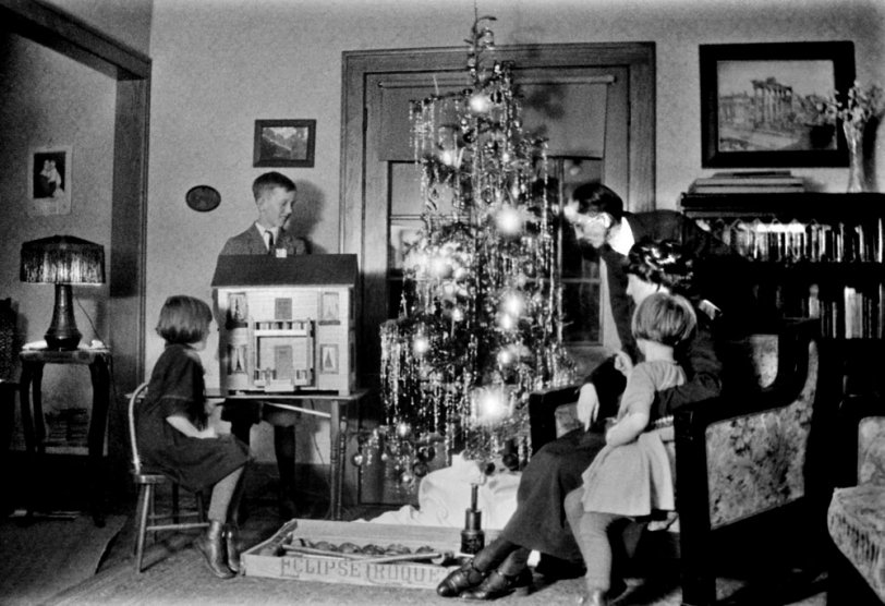 Toledo, OH (approx 1924) - It's been at least a dozen years since "Christmas in Buffalo: c. 1910."  My Grandparents (Albert and Hedwig Happel) have had five children and buried the two oldest. In addition to the tinsel laden tree we see the doll house that my Grandfather built for his two daughters (Emily seated and Lee snuggling with her mother).  Their older brother Hermann stands behind the doll house. 
Many years later my father (Anton, born several years after this photo was taken) renovated the doll house for his daughters. It is currently in storage in my basement awaiting the day that I or my son renovate it so that another generation can play with it. View full size.
