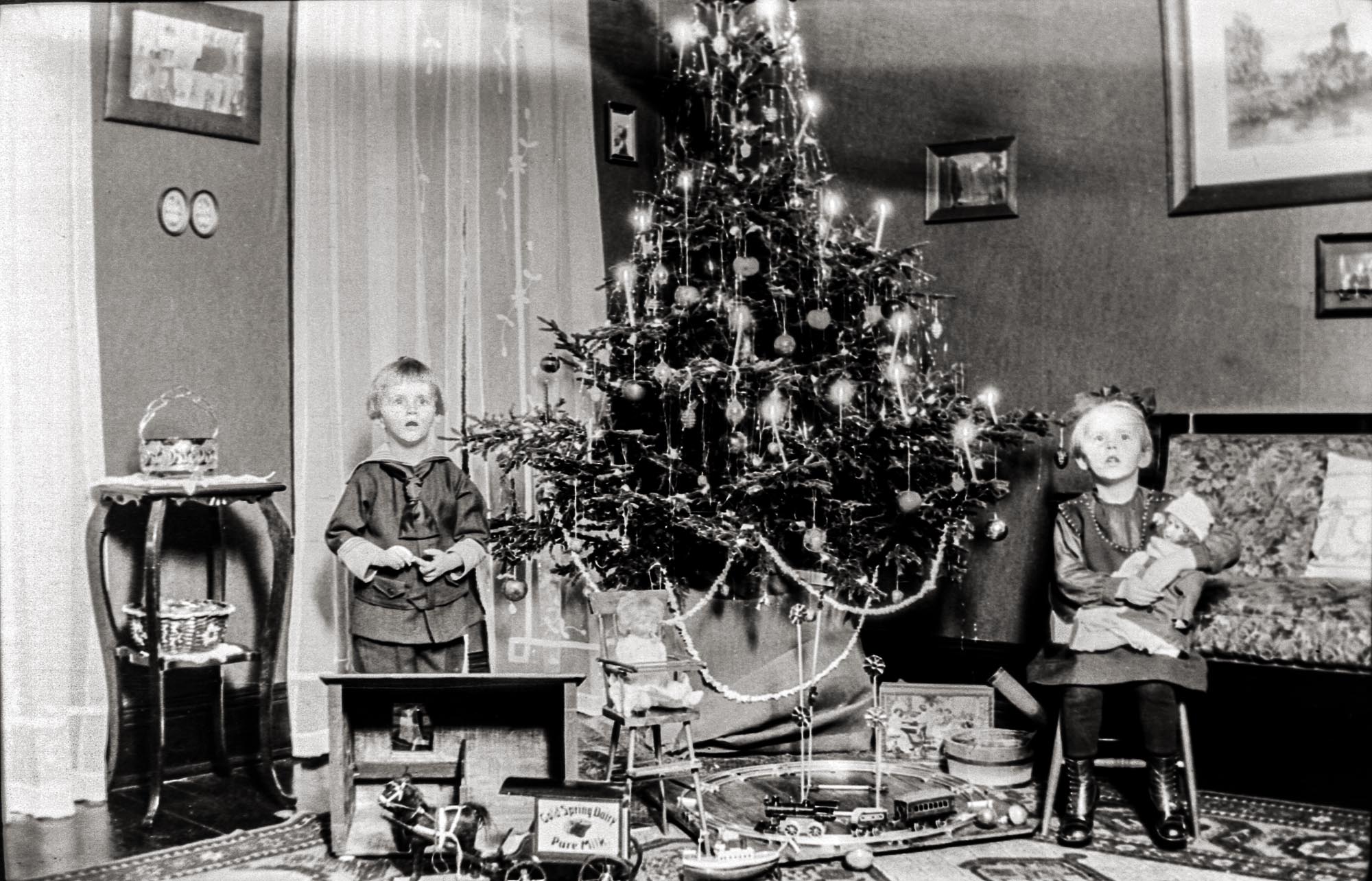 Christmas in Buffalo, NY. 1917. The year is a guesstimate based on the birth dates of Hermann (1912, on the left) and Johanna (1911).  They are enjoying their new toys under the tree lit with actual candles.

In additional to the traditional train by the tree I find most fascinating the horse-drawn milk delivery wagon.  This image doesn't show it well but the horse is mounted on a wheeled platform for smoother playtime.

This image was digitized from a 4x5 glass negative.