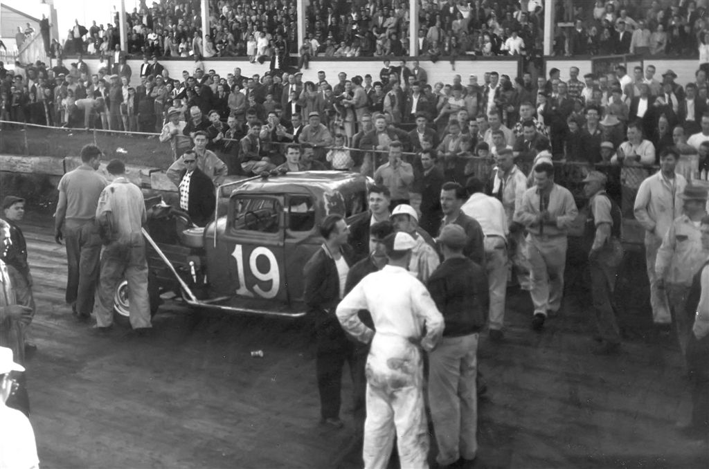 Local jalopy driver and fan favorite Louis T(white helmet) is always in some kind of trouble with the judges or with another driver.  Photo taken circa 1954 at the CLE fairgrounds track in the middle of town, in Fort William Ontario Canada, now Thunder Bay, Ontario.  The best days of my childhood life. View full size.