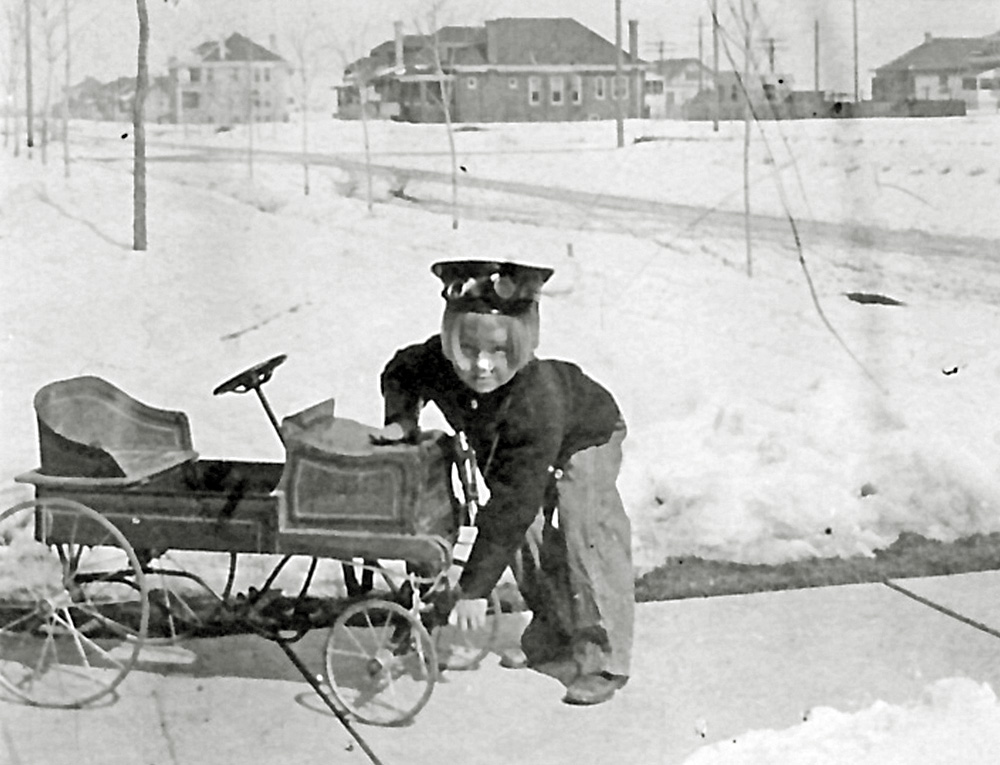 Denver Colorado 1909. Donald G. Kirk, my wife's dad, is hand cranking the car on a cold day. The make and model are unknown. The probable location is somewhere on Eudora street.