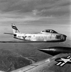 This photo was taken on a flight from Van Nuys, Calif., to Palmdale, Calif., in 1954. I was in the Air National Guard from 1948 to 1957. View full size.
Korean War survivor This F-86, 48-260, saw combat against MiG-15s in Korea, flying most of its missions from Kimpo Air Base in Seoul. It was assigned to the 4th Fighter Wing, the first F-86 unit in Korea. At some point after its California Air National Guard service (dclark26's photo, above) it spent years at the Smithsonian's Paul Garber restoration facility in Maryland. Since 2005 it has been on display at the Udvar-Hazy Center of the National Air and Space Museum near Dulles airport in Virginia. Here's a portion of a picture I took of it in 2009, showing its 48-260 serial number. Its history can be found on Joe Baugher's fantastic archive of U.S. military aircraft http://www.joebaugher.com/usaf_serials/1946.html
Full History of s/n 48-260In fairness Baugher's site isn't very detailed. The full (ish) history of this machine is thus:
F-86A-5 s/n 48-260 with construction number 43629.
Delivered 26 July 1949
Assigned to 4th Fighter Group 31 July 1949
To 334th FIS 15Aug50
Assigned to 4th FIW 14 September 1950
To 13th Aircraft Repair Sqn Kisarazu (Japan) 28 January 1952
To 6400th Air Depot Wing FEAMCOM 31 January 1952
To 4th FIW, Korea 20 February 1952
To 6400th ADW FEAMCOM 27 April 1952
To San Francisco Air Materiel Command 7 June 1952
To Sacramento Air Materiel Area, McClellan AFB CA 10 June 1952
To North American Aviation Fresno 11 August 1952
To 3595th Combat Crew Training Wing, Nellis AFB 26 May 1953
To Sacramento Air Materiel Area 7 January 1954
To 116th FIS Washington ANG 6 February 1954
To 195th FIS CA ANG (1954?) - though I think the above photo is with 115th FIS CA ANG.
To Boeing December 1957
To NASM 25 January 1962
F-86A 48-260This aircraft was with the 195th. It had the checker board painted nose.
Aircraft recordsIn fairness to Joe Baugher, if each of his 92 gazillion listed aircraft had a record as detailed as the excellent one Sabrejet provided, he'd need another Internet. Also, a lot of his info comes from contributors to his site who appreciate his efforts to archive as many military aircraft as possible. I'm one of them and have sent him probably at least a hundred records through a number of years. Without such sites there'd be no record of many, many specific airplanes that men flew and, too often, died in.  
And the other aircraft is......judging by the fixed fuel tanks on the end of the wing, the photo was taken from an F-89 Scorpion. 
(ShorpyBlog, Member Gallery)