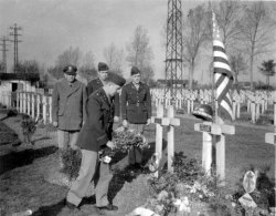 American soldiers during World War II are placing a wreath on a grave that has a US helmet hanging from it, with the words, Egalite, Fraternite, painted on it, and _57th Inf. and what looked like a divisional emblem.
After looking at the photo with my jeweler's Loupe I was able to make out that the divisional emblem on the helmet was that of the 90th Infantry Division - the _57th Inf. on the helmet is probably the 357th Infantry, which was part of the 90th Division during World War II.
I was also able to make out the name on the grave: John Schila Deming, and the words "Soldat Estranger" and the date 1917. After doing a little research online, I found the grave - John Schila Deming was born on March 24, 1884 in Columbus, Ohio. He joined the French Foreign Legion after having previously served for a brief time in the Canadian Army. He was killed in June 22, 1917, and is buried in the French Military Cemetery at Cormicy. According to the Cormicy website, he was killed at Vaux Varennes (if I was reading the translation of the French website correctly). View full size.
(ShorpyBlog, Member Gallery)